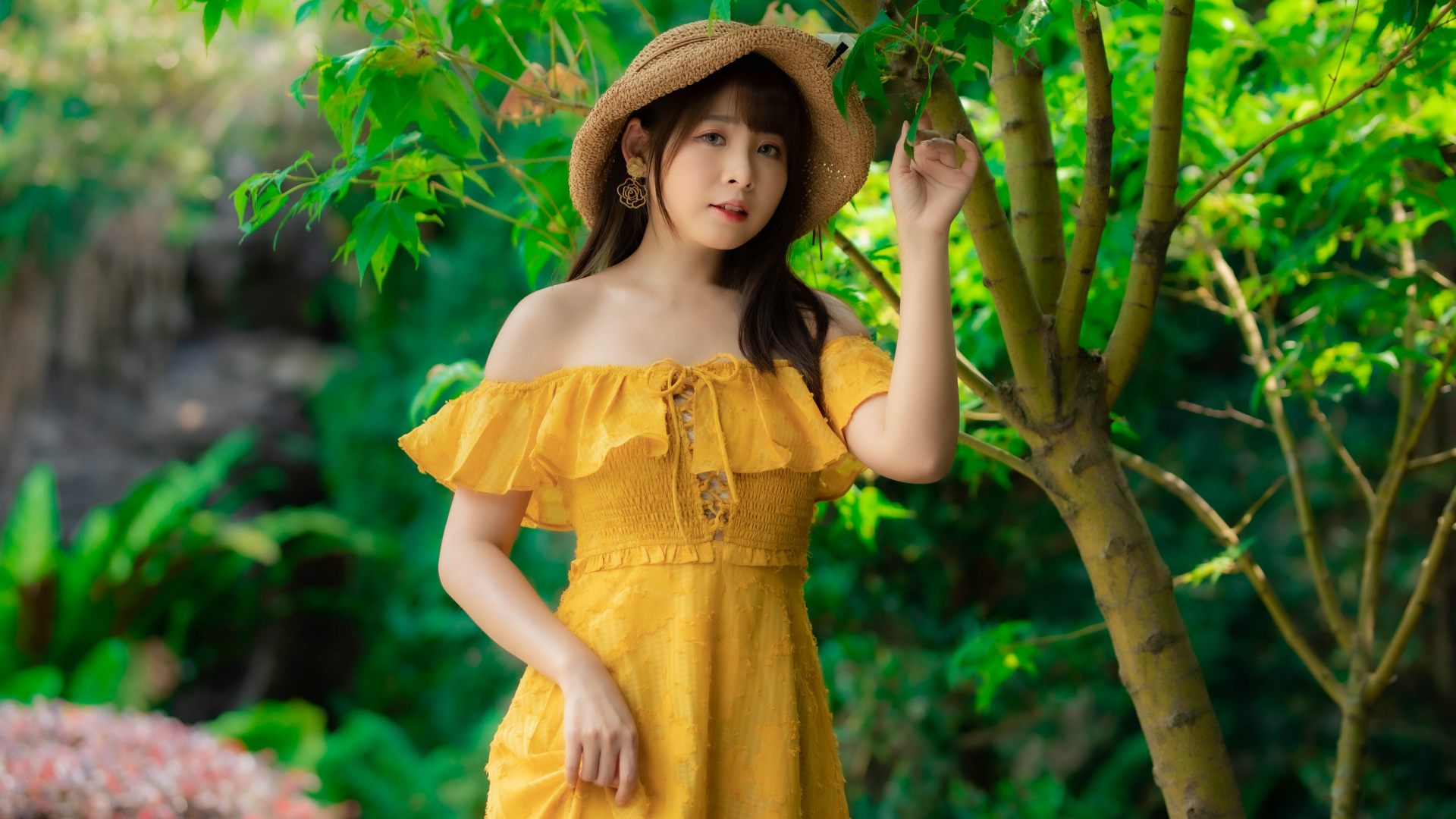 Красивая девушка азиатка в желтом платье   шляпе у дерева