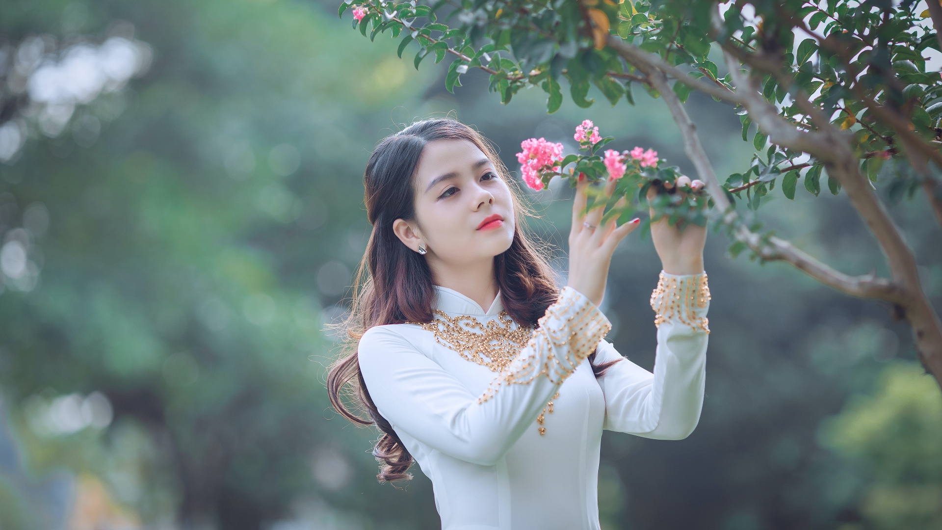 Красивая азиатка в белом платье у ветки с розовыми цветами