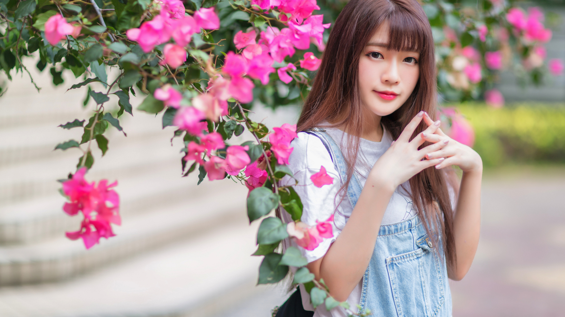 Красивая милая азиатка стоит у куста с розовыми цветами