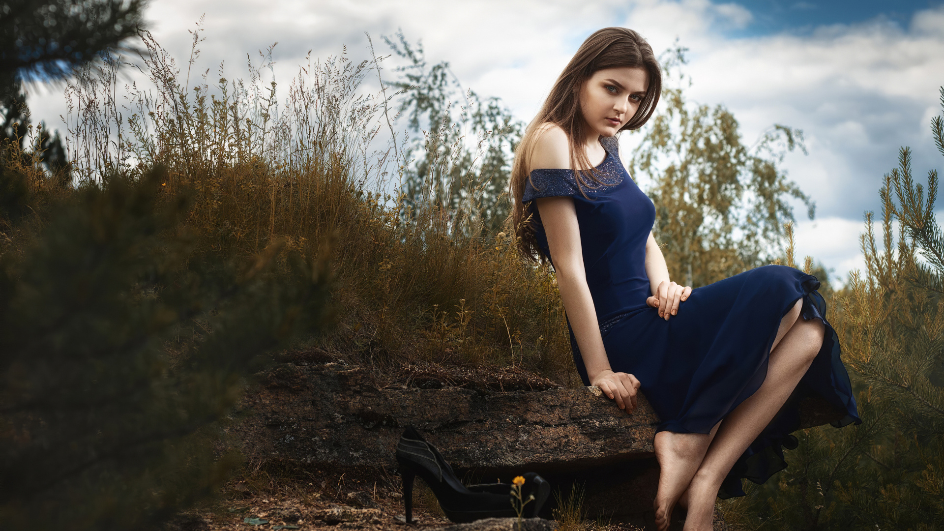 Красивая девушка в длинном синем платье сидит на камне 
