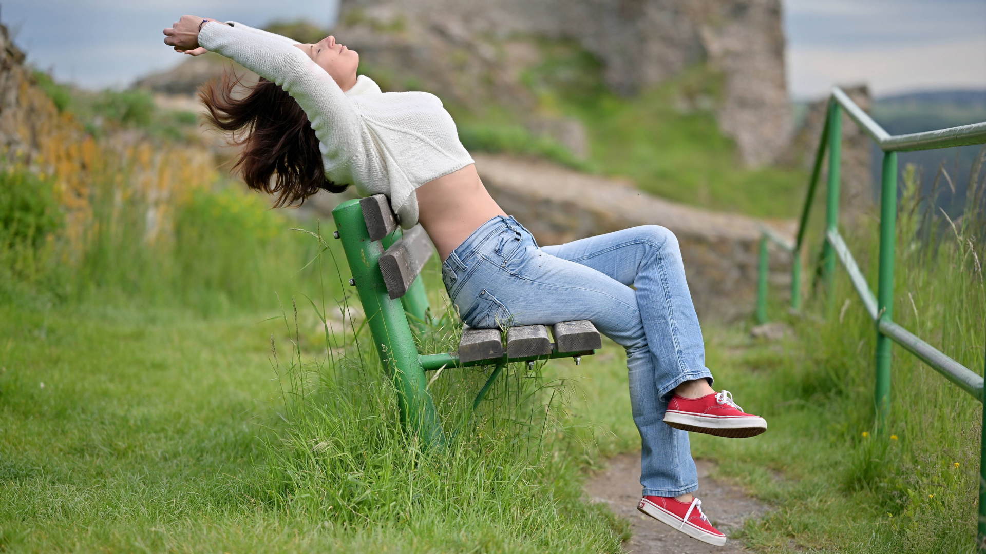 Девушка в синих джинсах сидит на лавке 