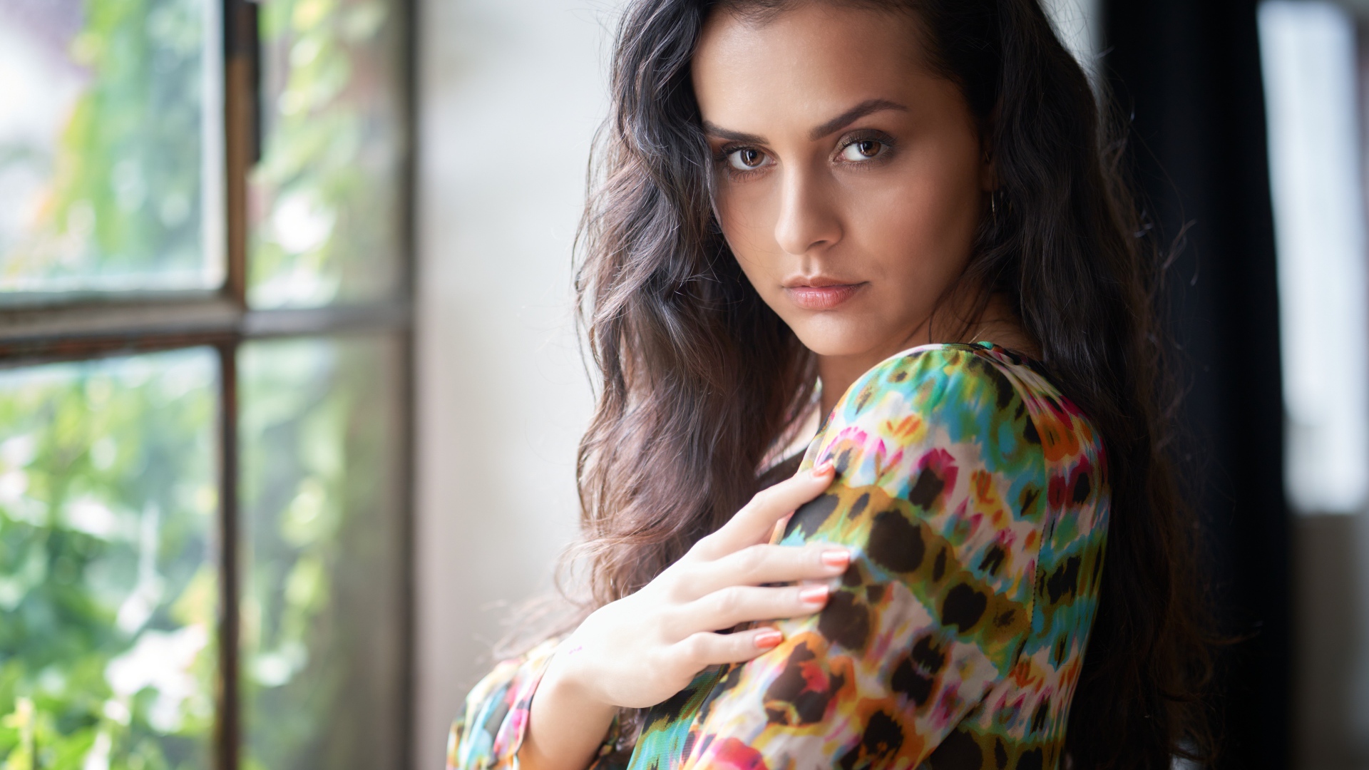 Длинноволосая кареглазая девушка стоит у окна