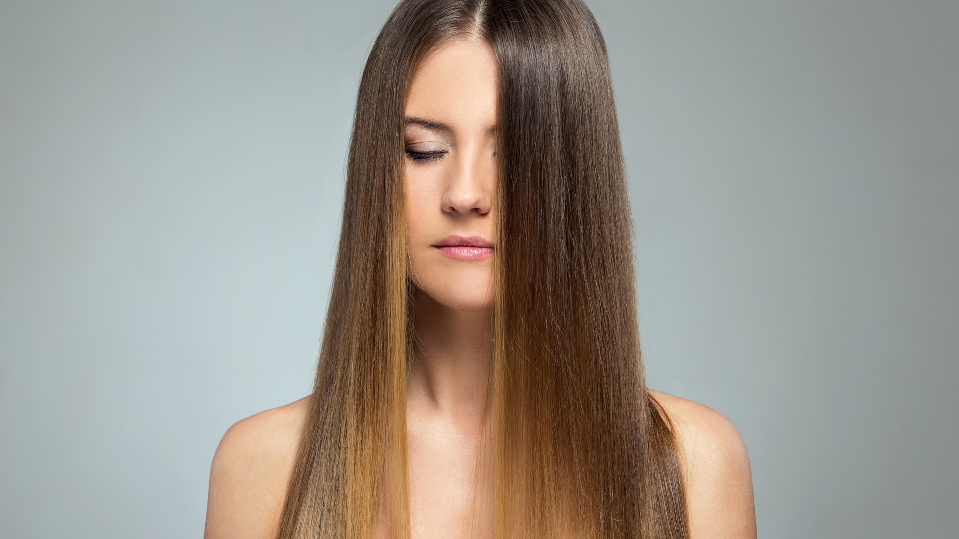 Длинноволосая шатенка с закрытыми глазами на сером фоне 