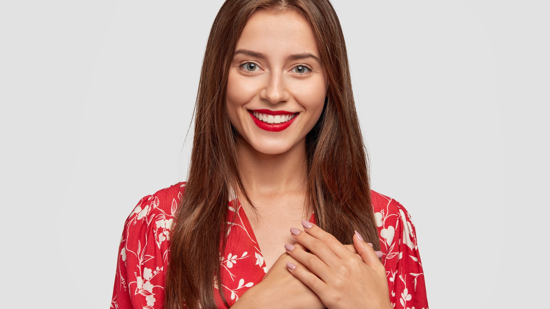 Улыбающаяся девушка с руками на сердце на сером фоне