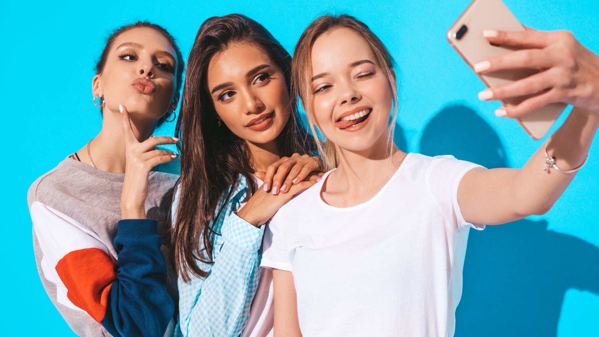Три подруги делают селфи на голубом фоне