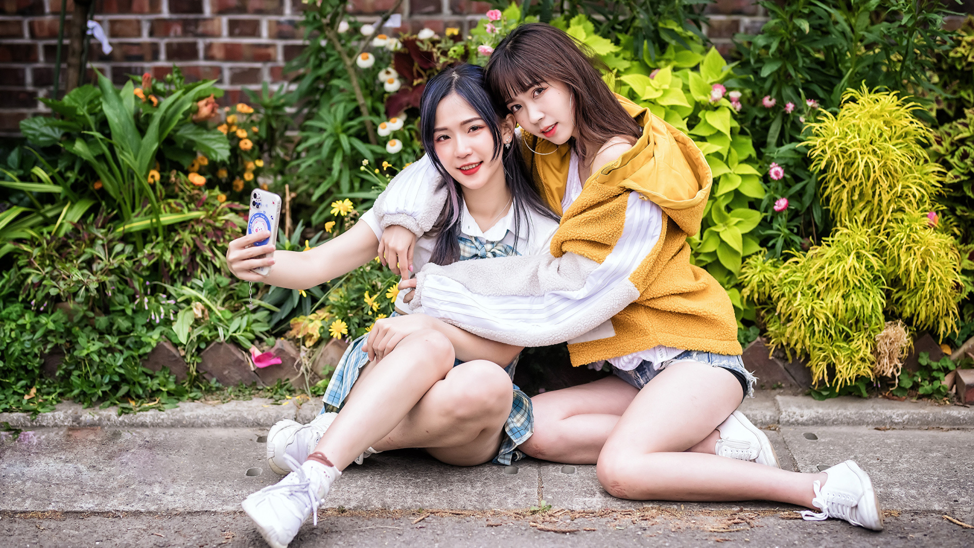 Две девушки азиатки сидят у стены с цветами 