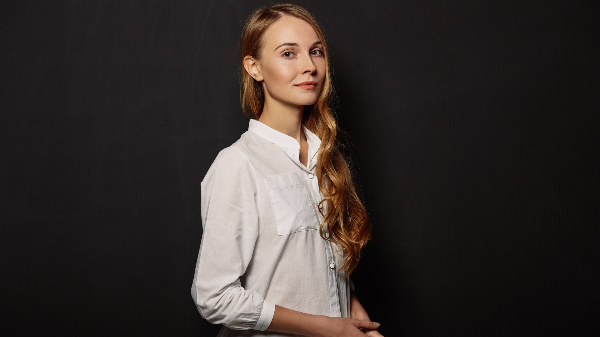 Молодая девушка в белой рубашке на фоне черной стены 