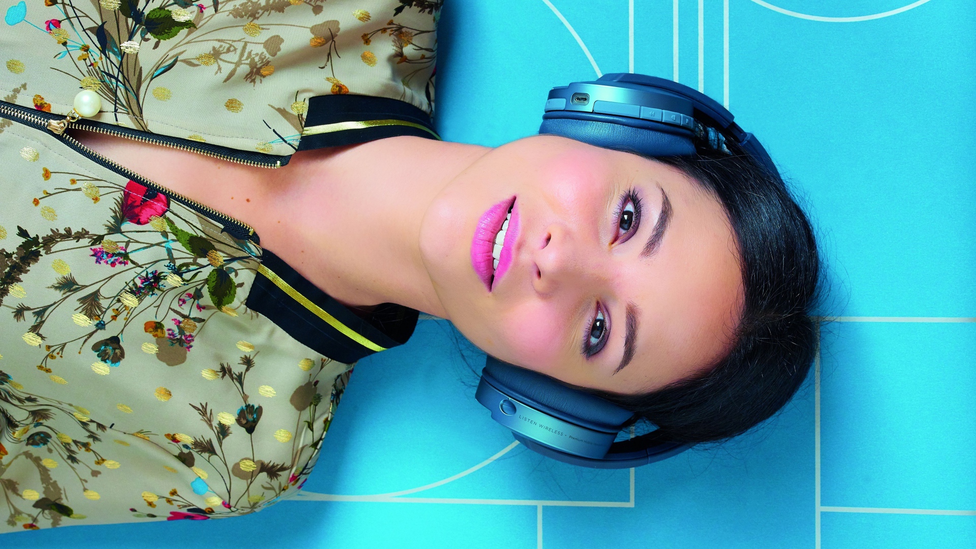 Молодая женщина в наушниках лежит на голубом полу