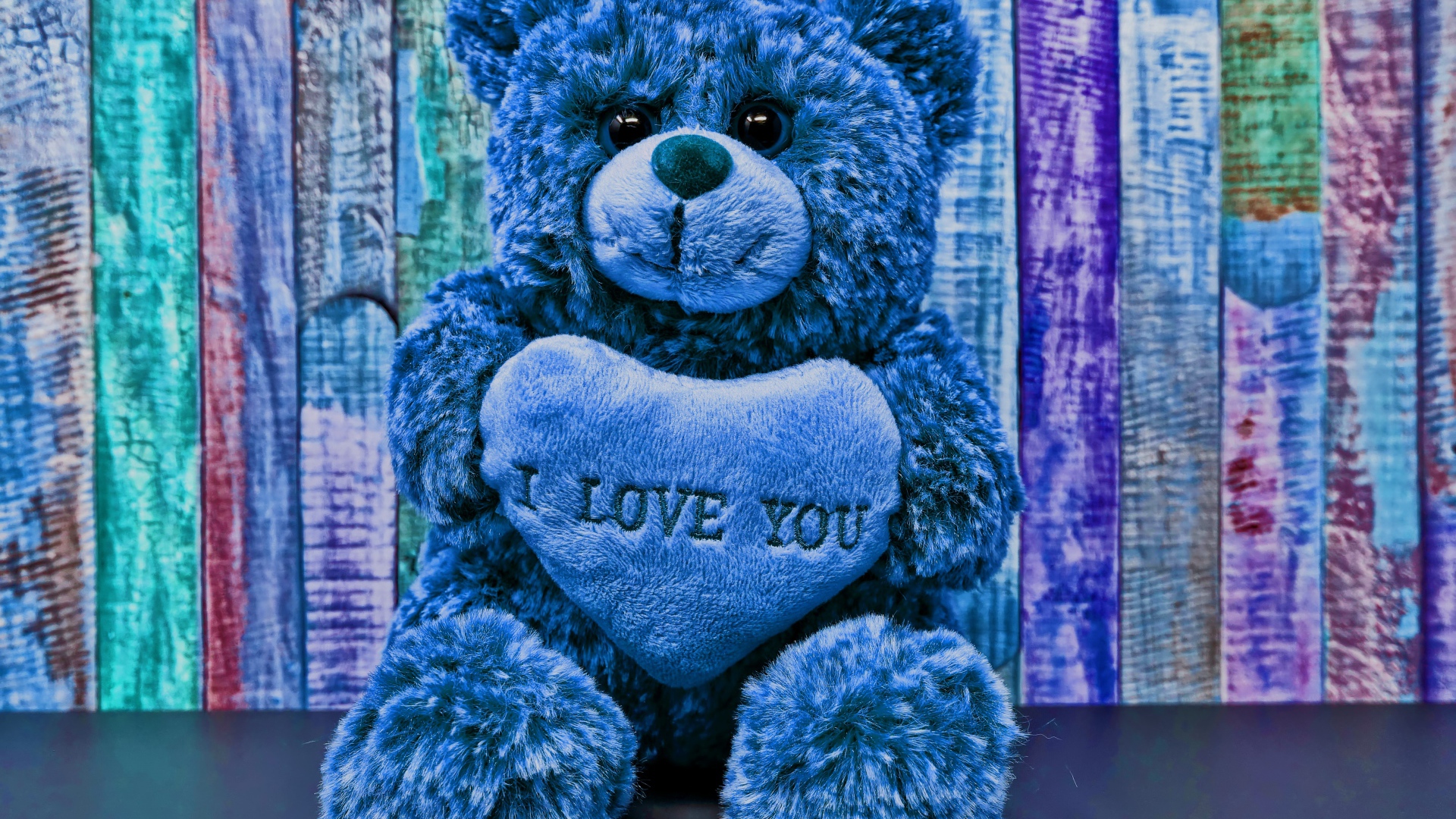 Синий медведь с сердцем на фоне забора