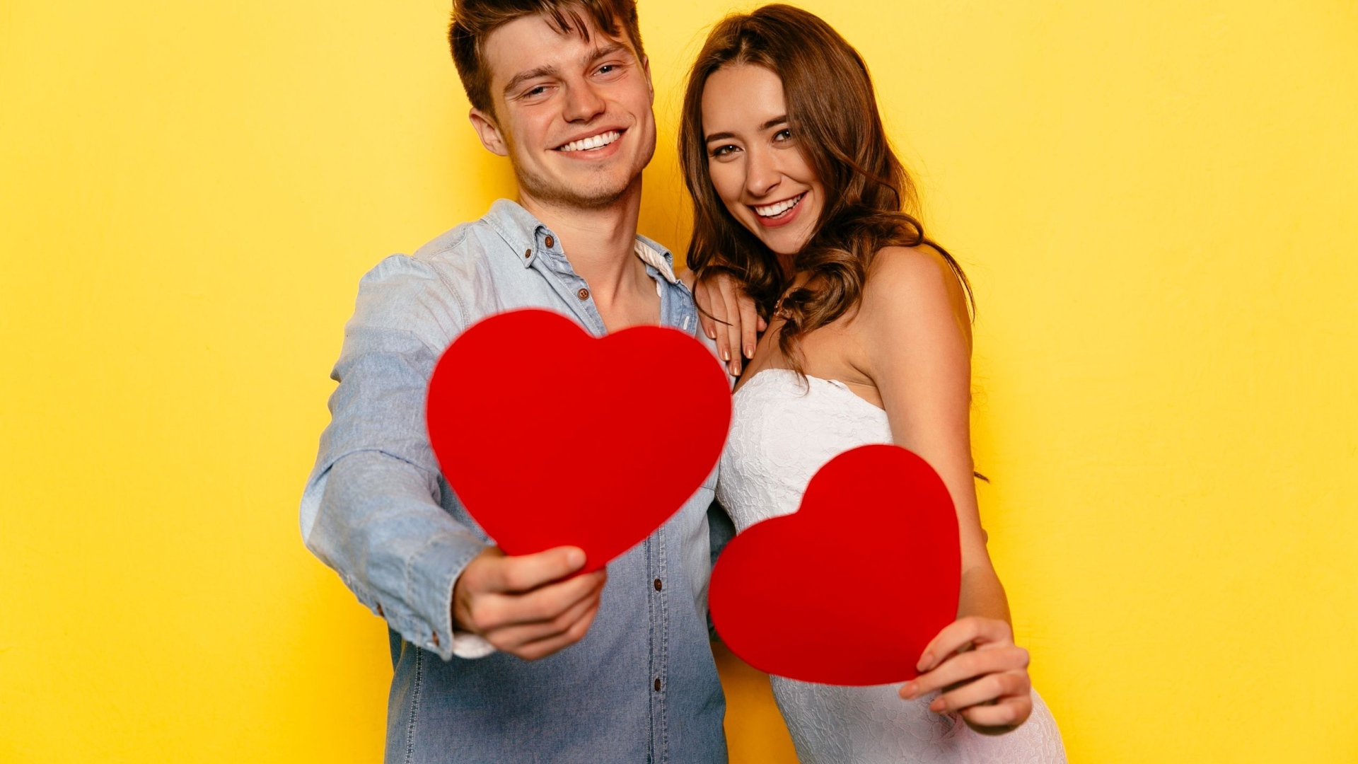 Влюбленная пара на желтом фоне с бумажными сердечками в руках 