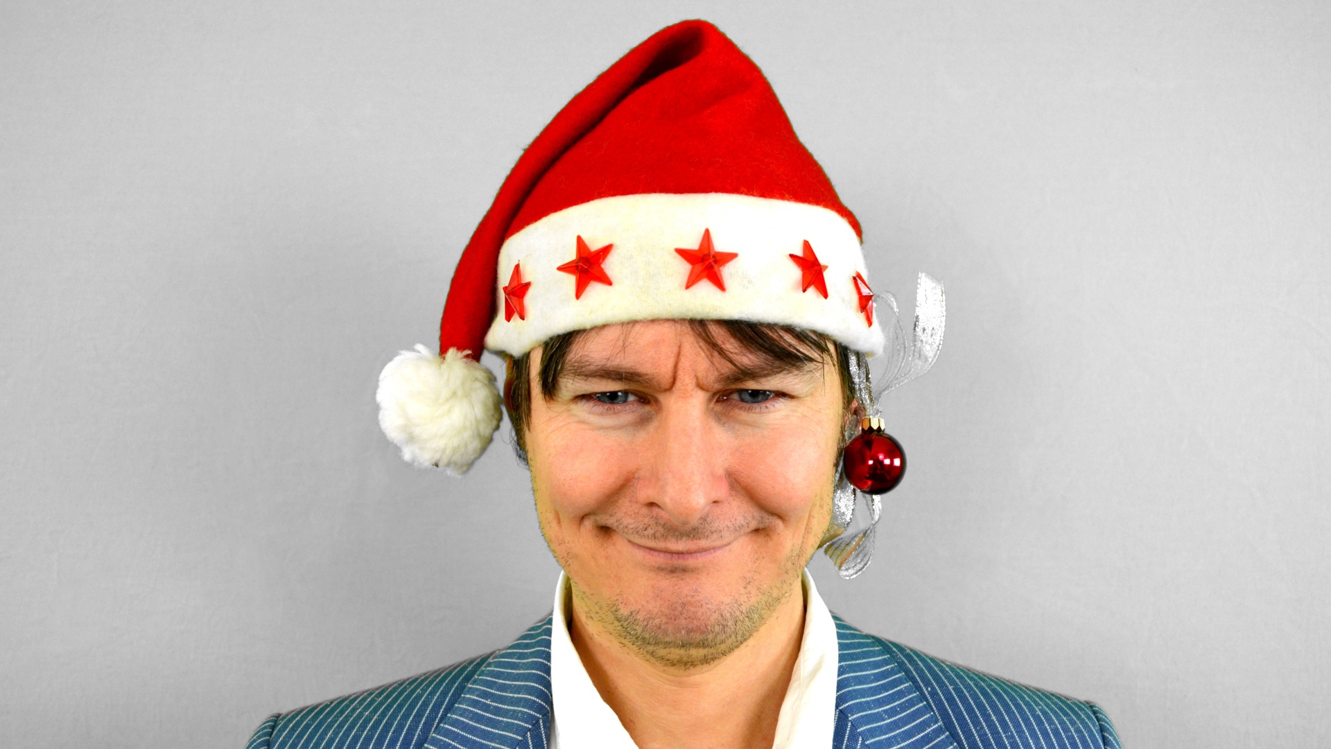 Голубоглазый мужчина в новогодней шапке на сером фоне 