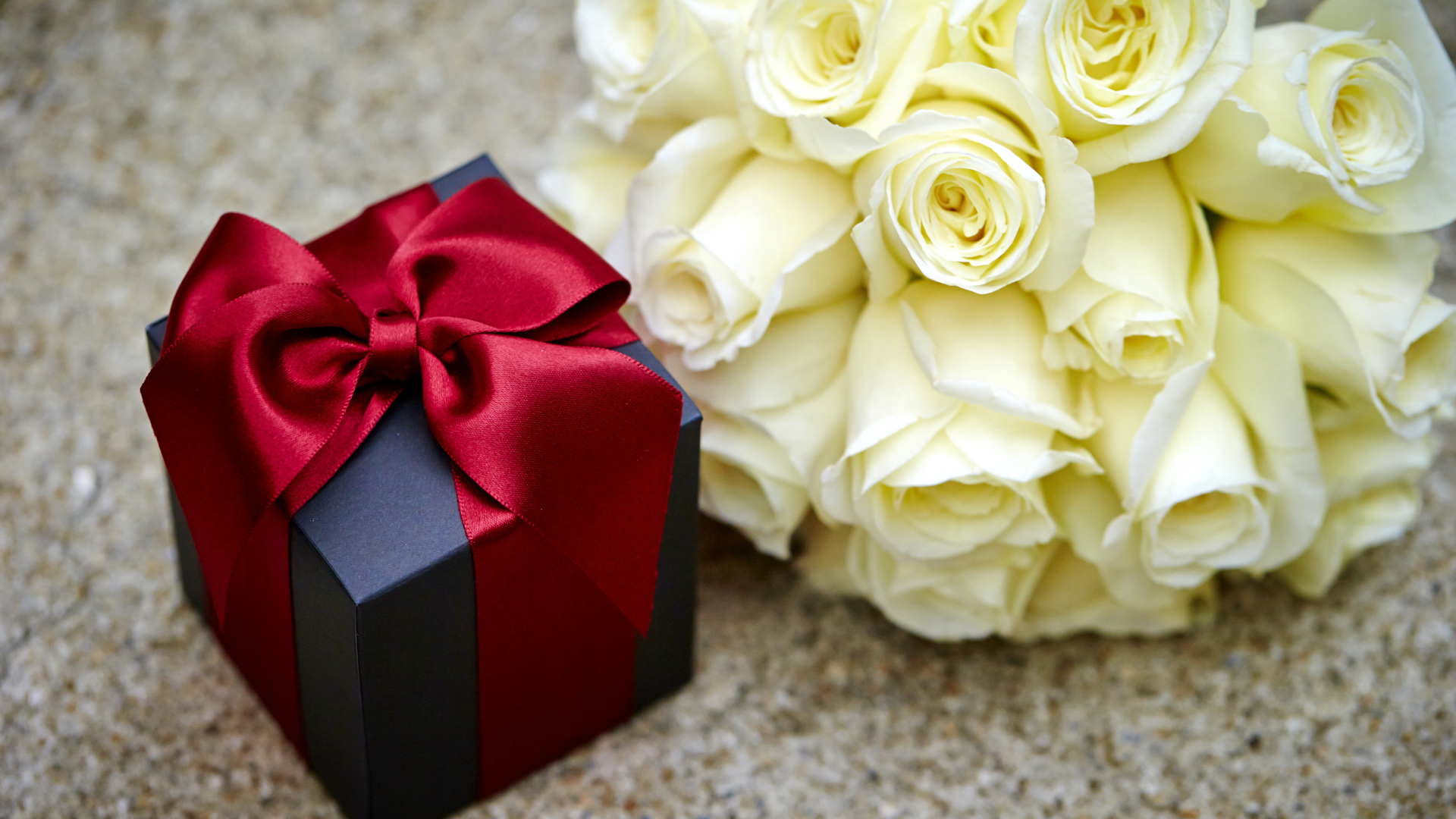 Букет белых роз с черным подарком на столе