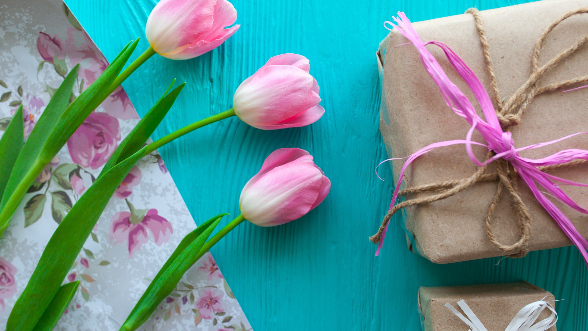 Три розовых тюльпана на голубом столе с подарками