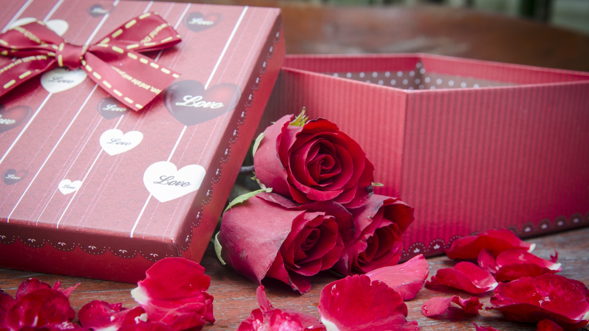 Три красные розы с лепестками  на столе с подарком