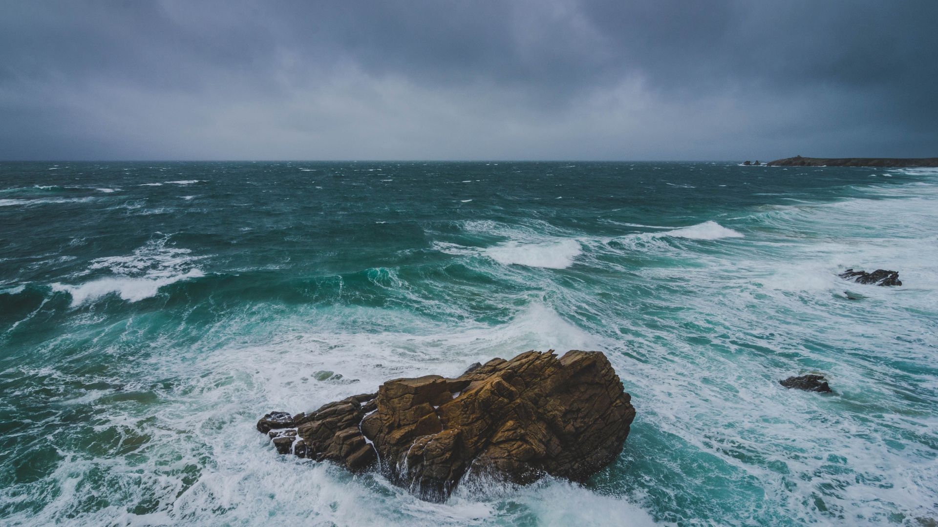 Большой камень омывают белые волны океана 