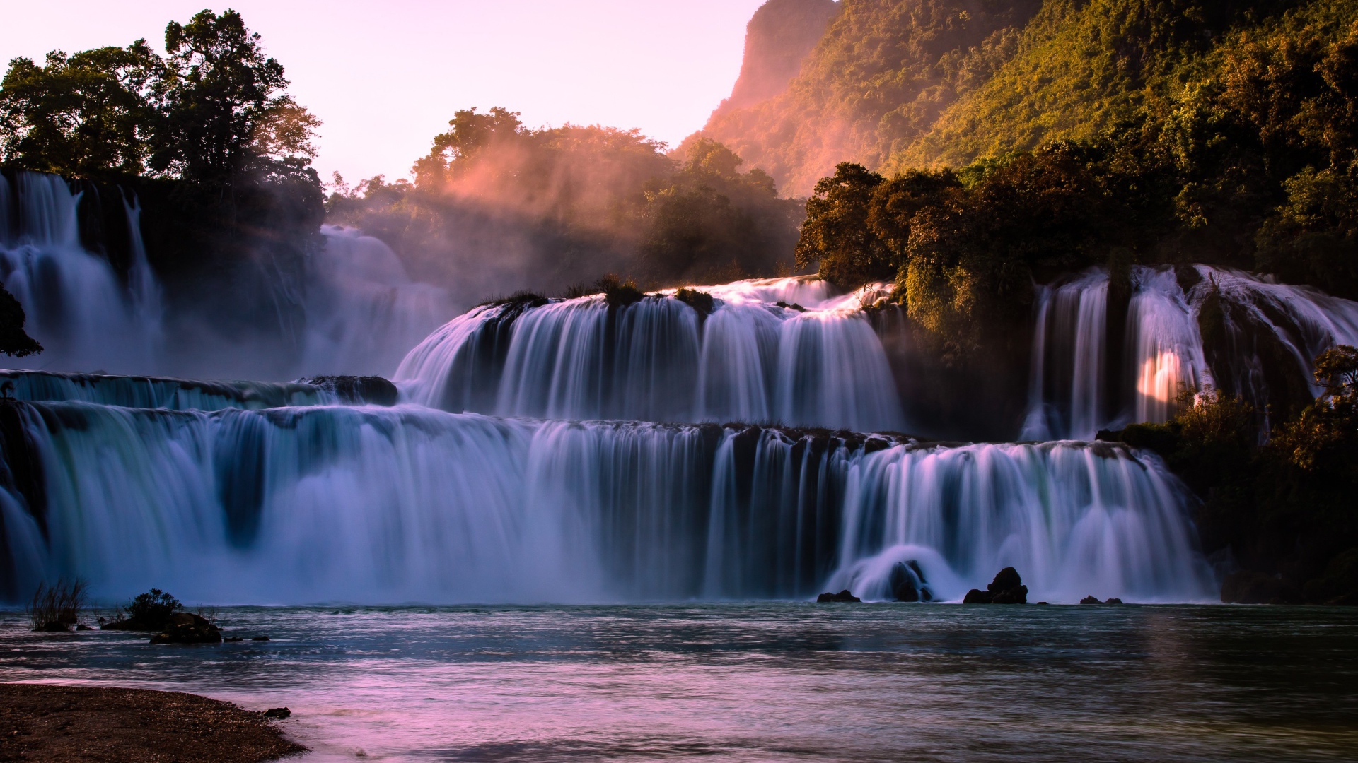 Каскадный водопад стекает по камням в лучах солнца 