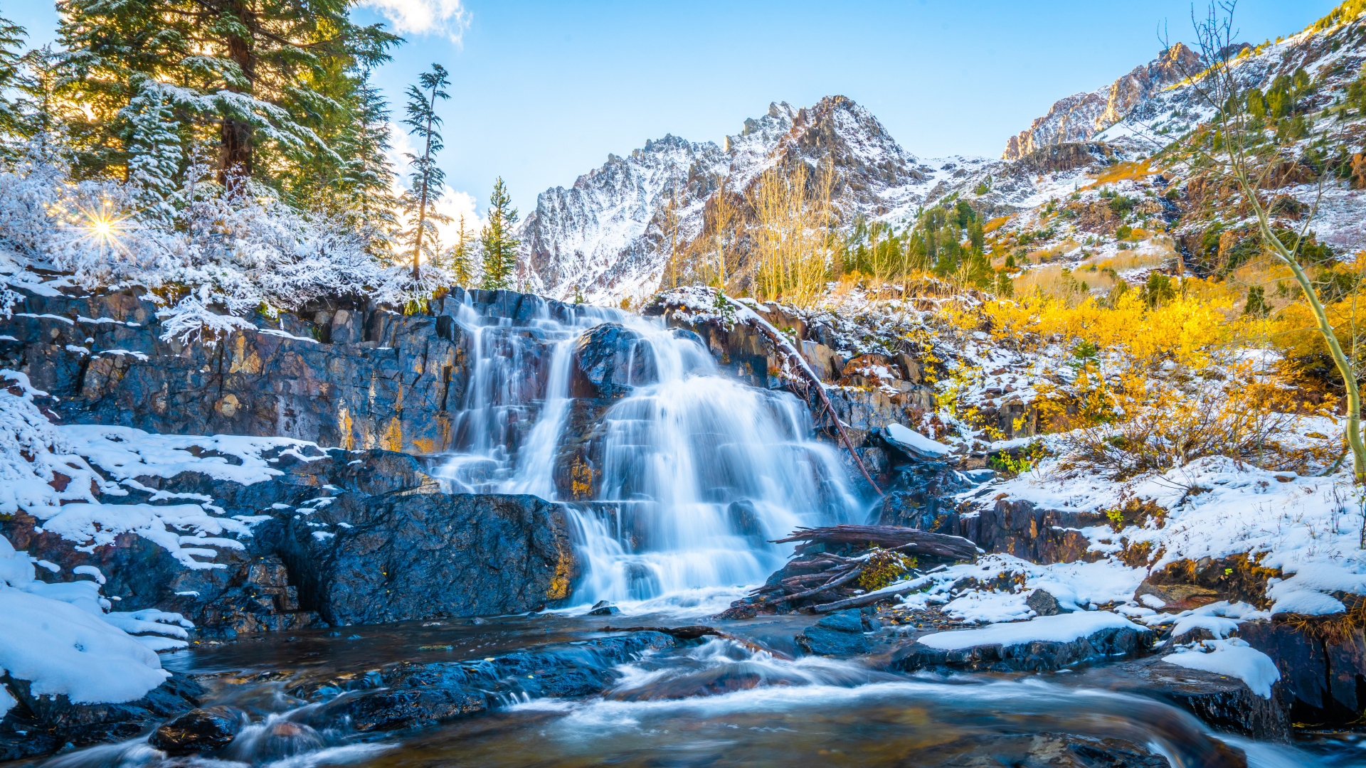 Водопад стекает по покрытым снегом камнях в горах