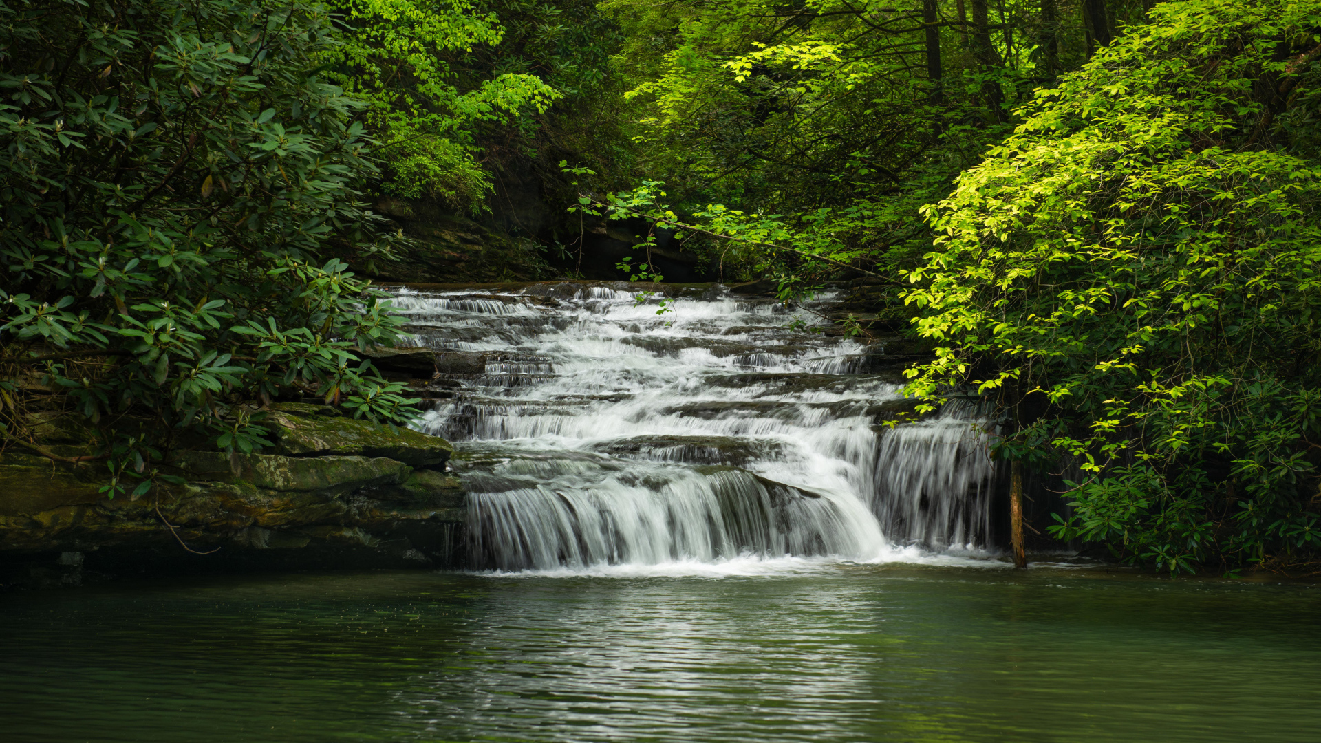 Водопад стекает по каменному каскаду в реку 