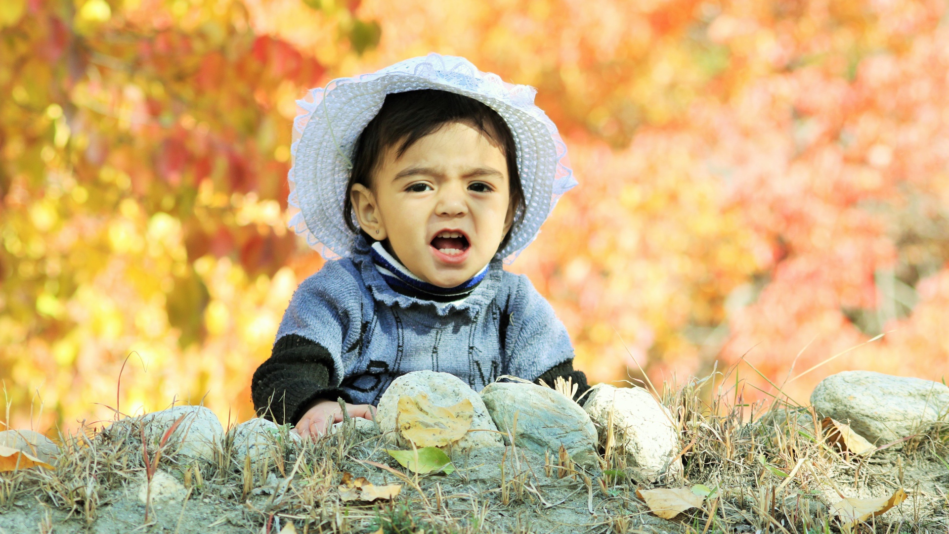Маленькая девочка в шляпке сидит на земле