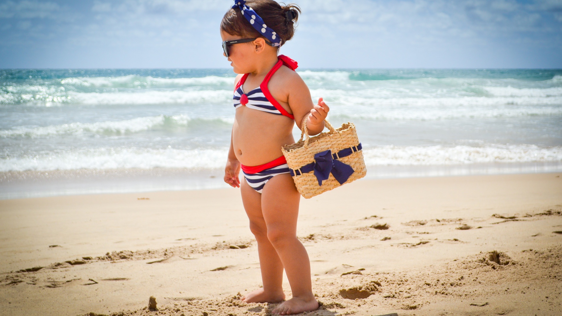 Маленькая девочка в купальнике гуляет по пляжу 
