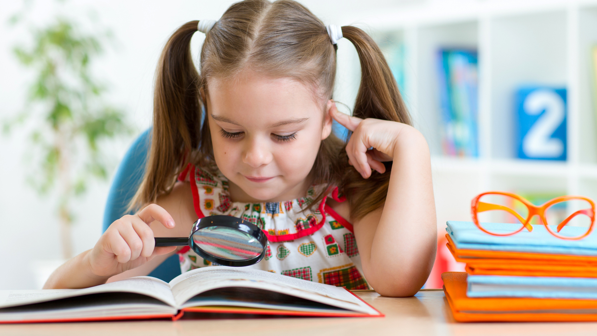 Маленькая девочка читает книгу с увеличительным стеклом 