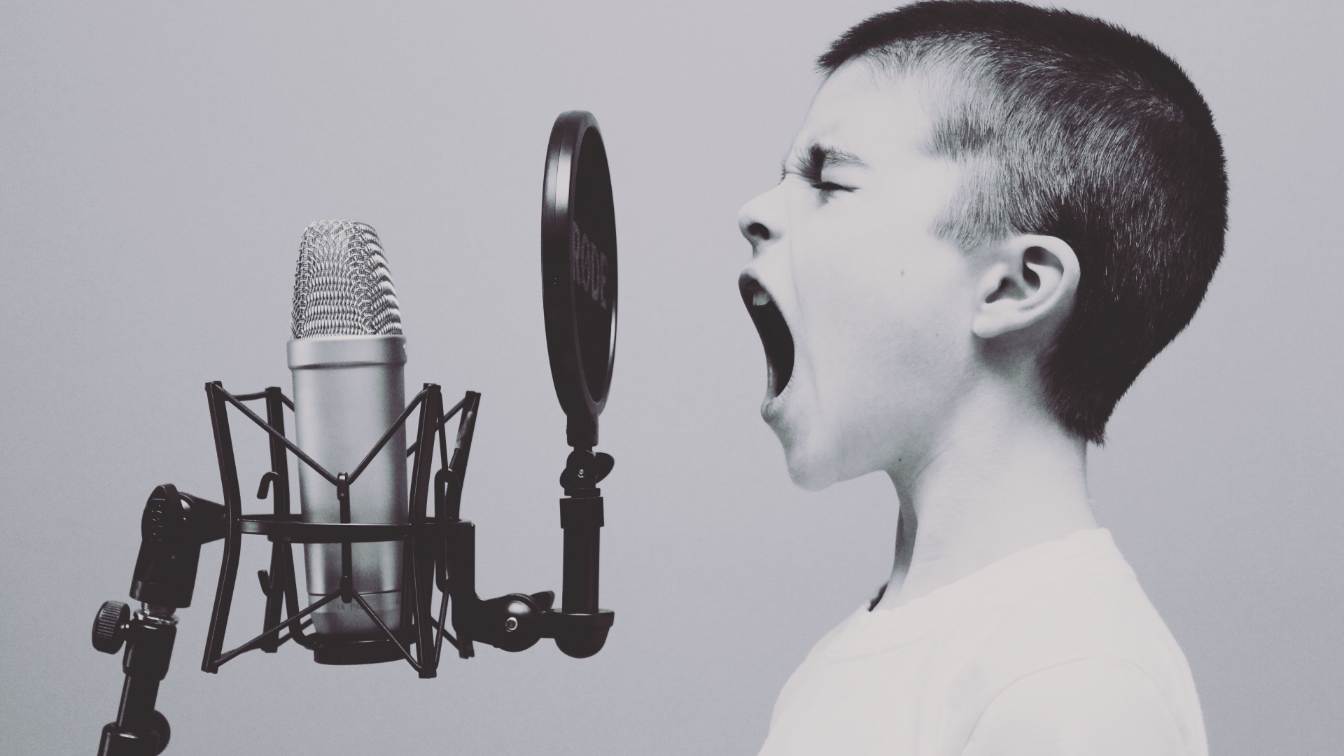Мальчик кричит в студийный микрофон на сером фоне 