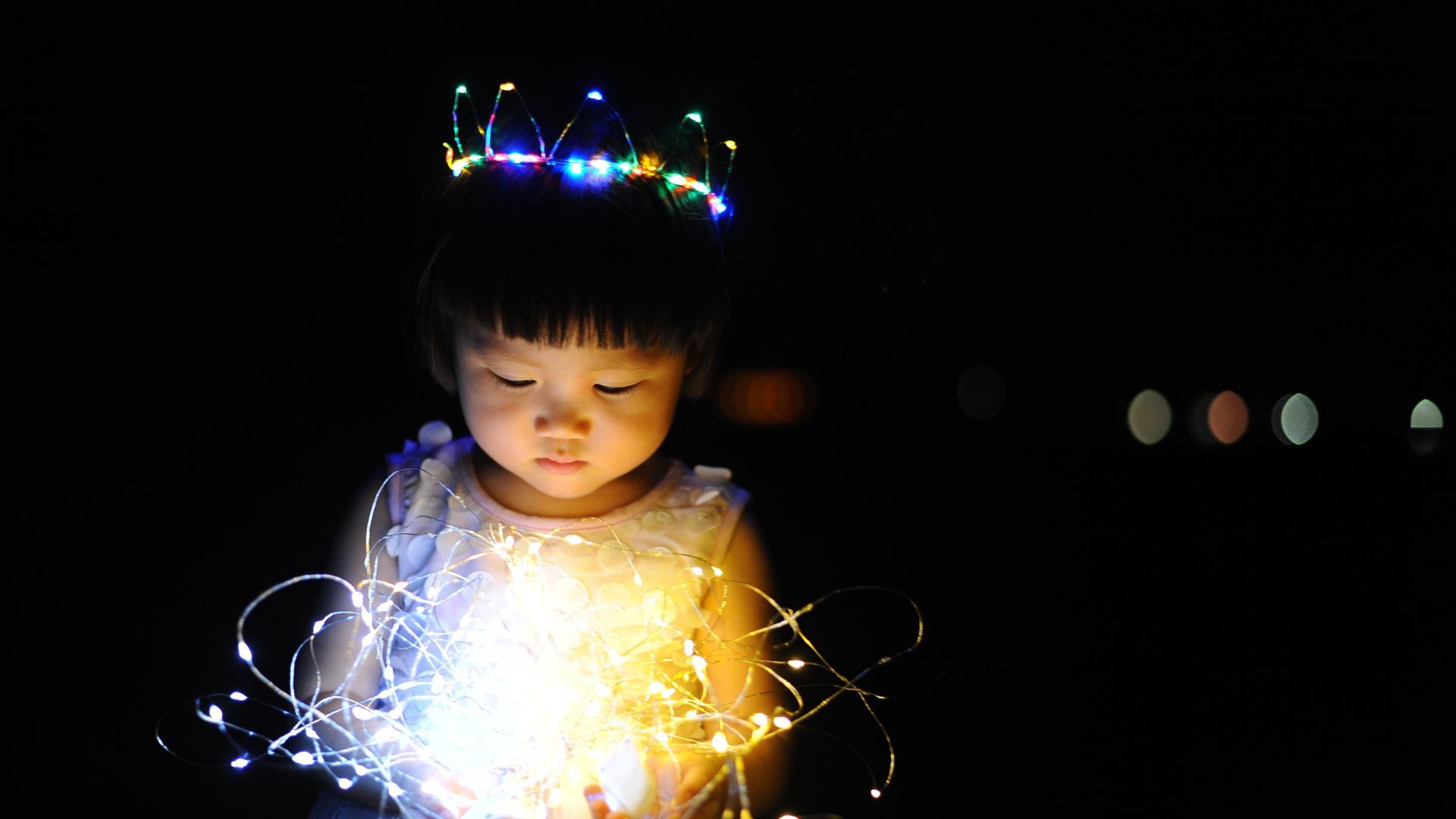 Маленькая девочка азиатка с гирляндой в руках на черном фоне