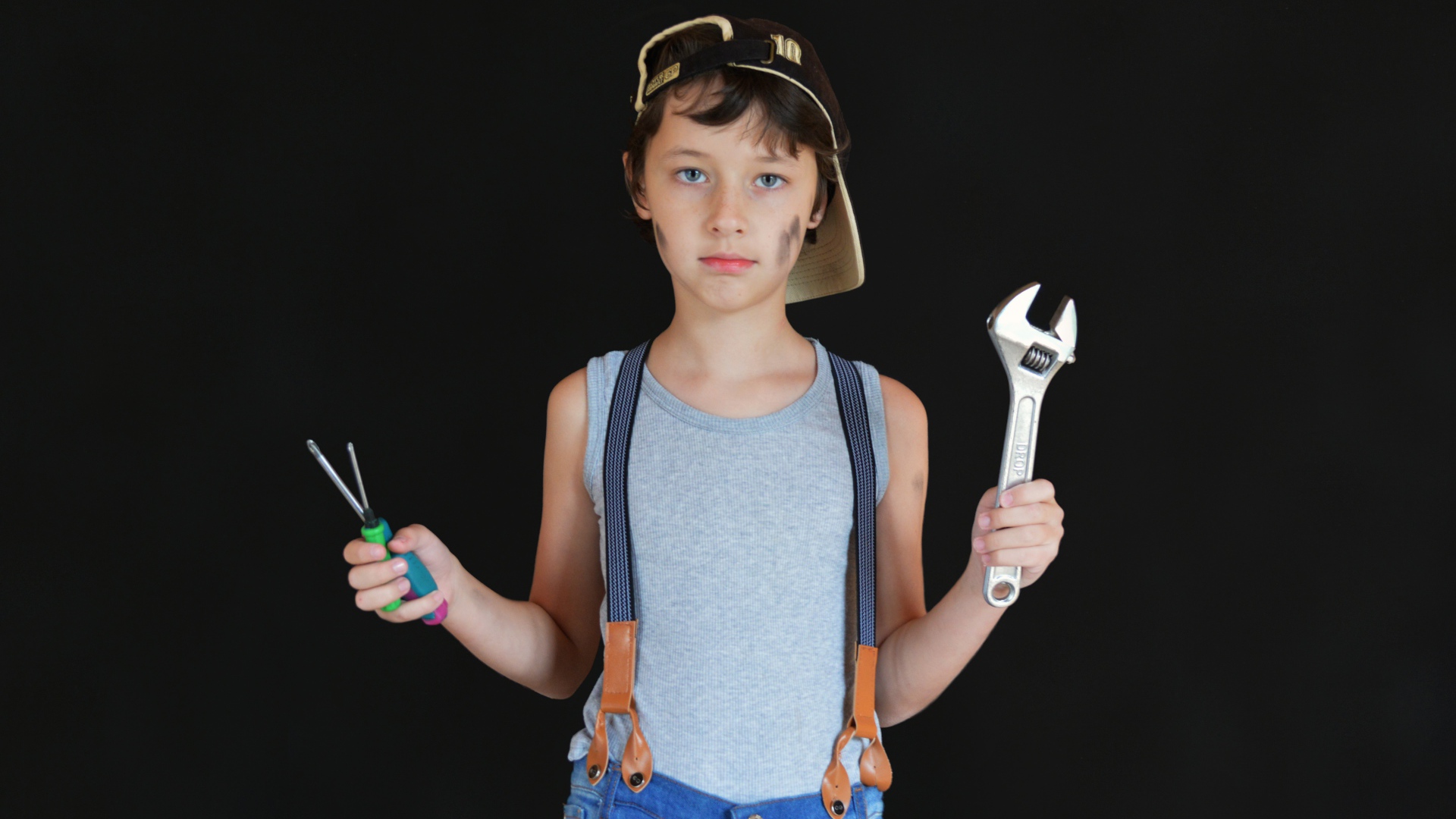 Маленький мальчик с инструментами в руках на черном фоне