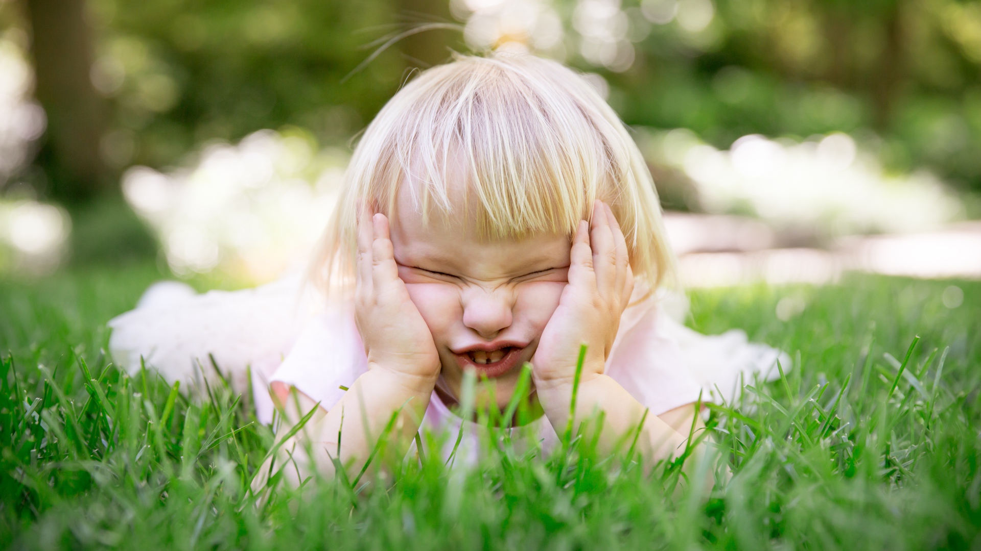 Маленькая смешная девочка лежит на зеленой траве 