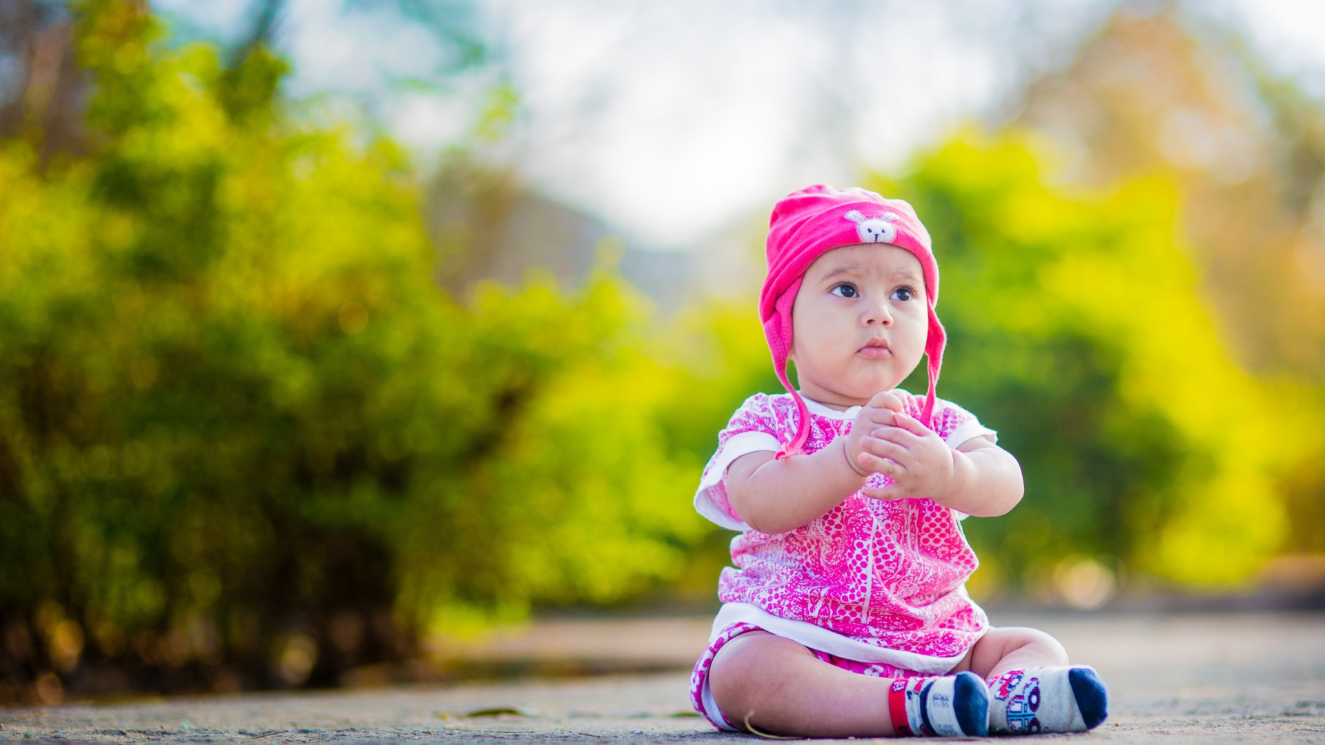 Маленькая девочка в розовом костюме сидит на земле