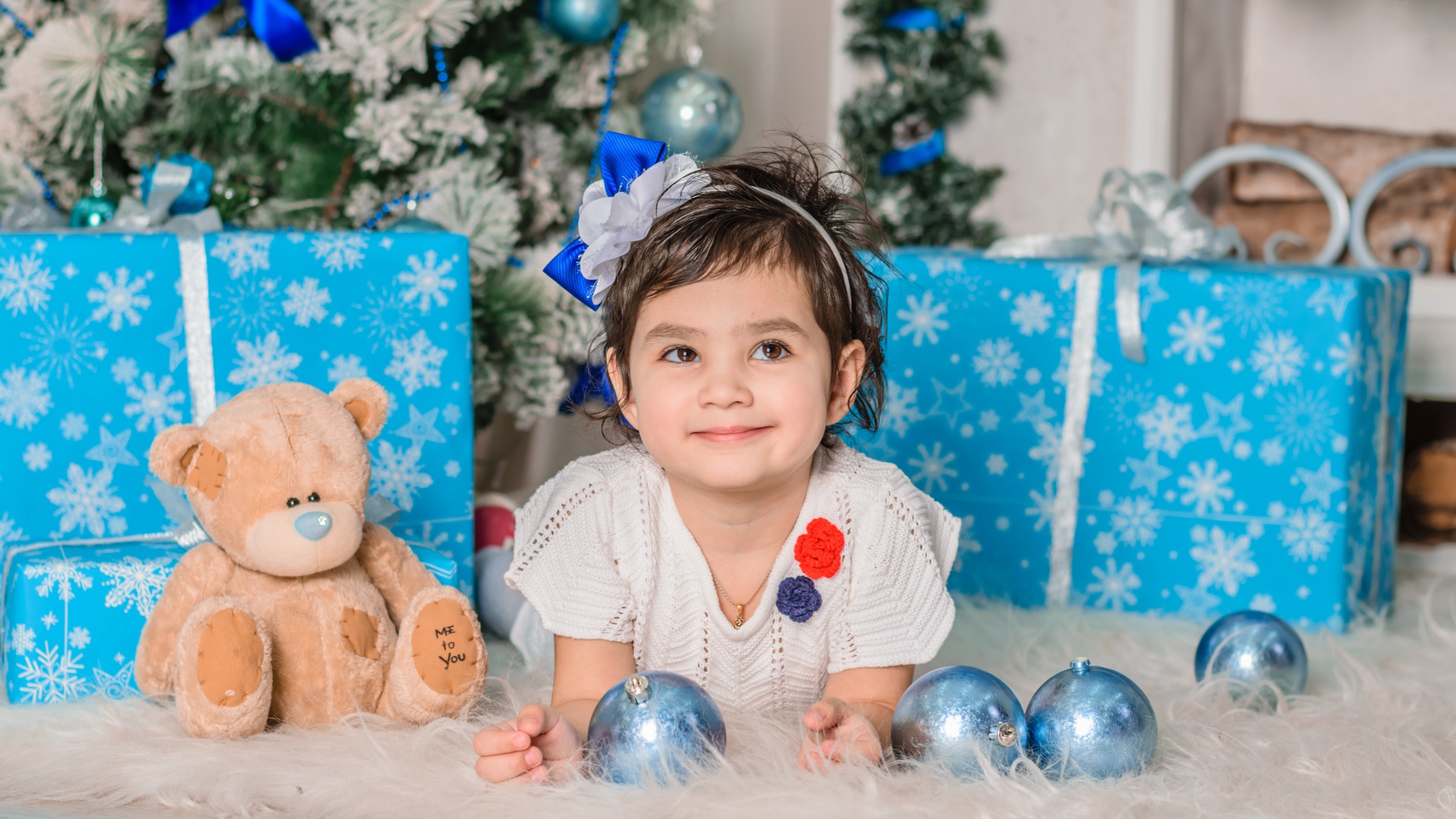 Маленькая девочка с подарками и игрушками под елкой 