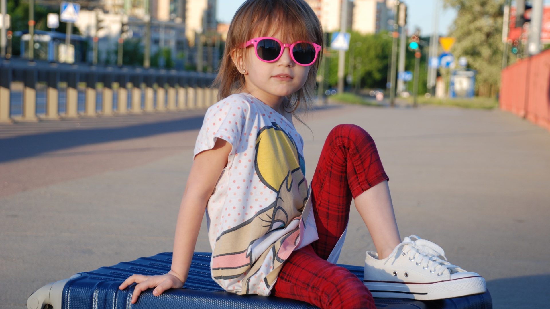 Маленькая девочка в очках сидит на чемодане