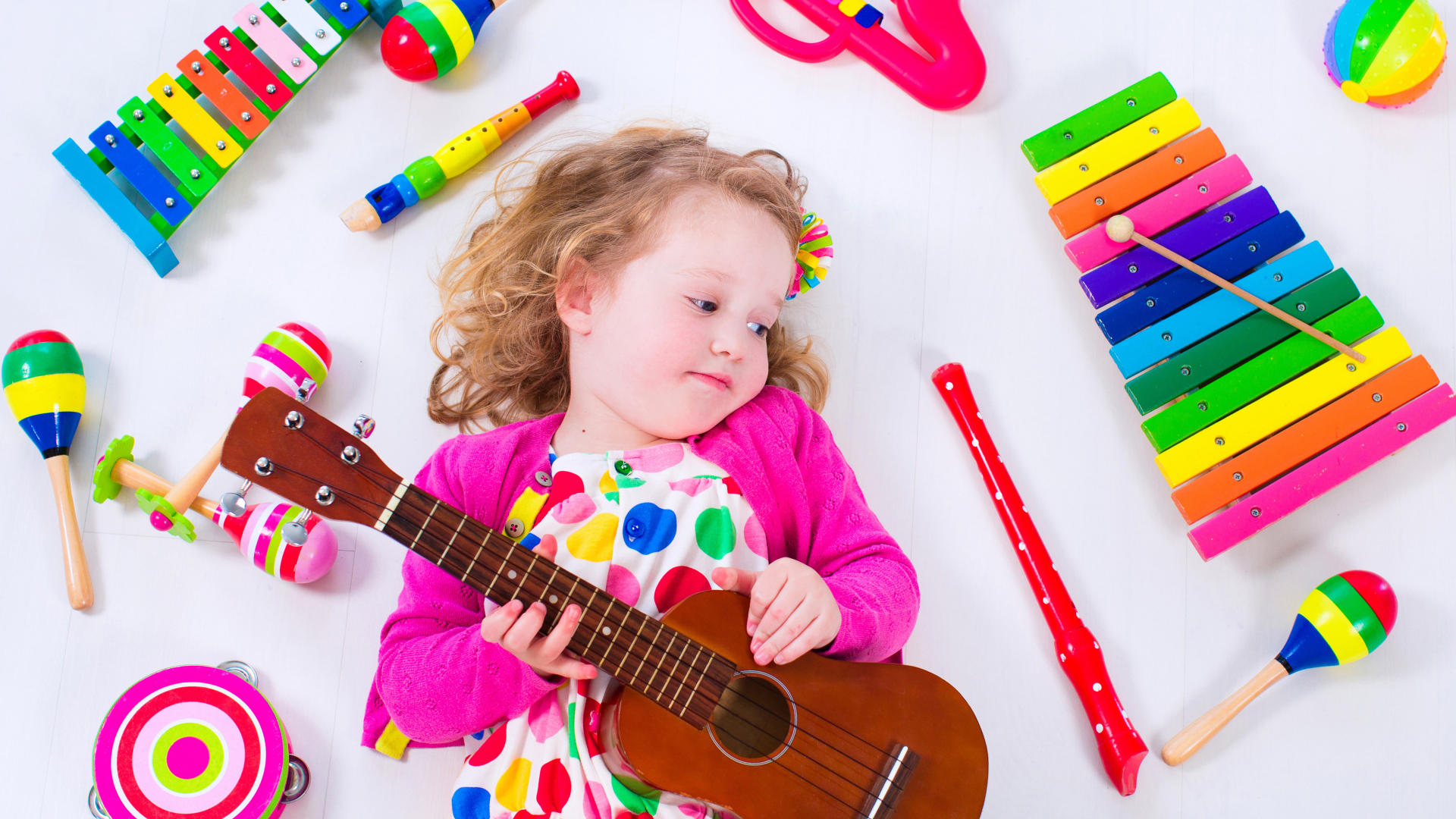 Маленькая девочка с гитарой и игрушечными музыкальными  инструментами 