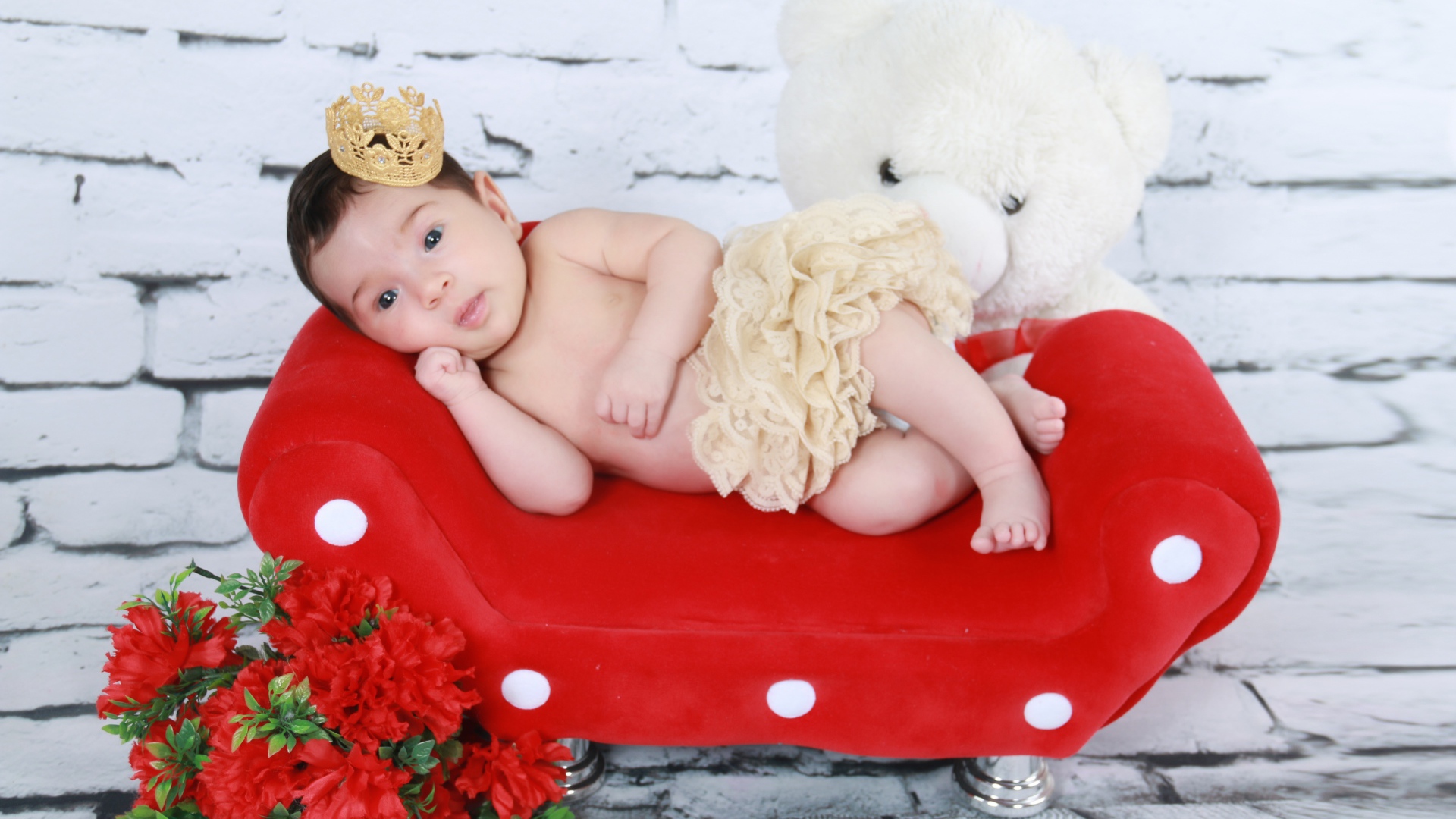 Маленькая принцесса лежит на красном диване у стены 