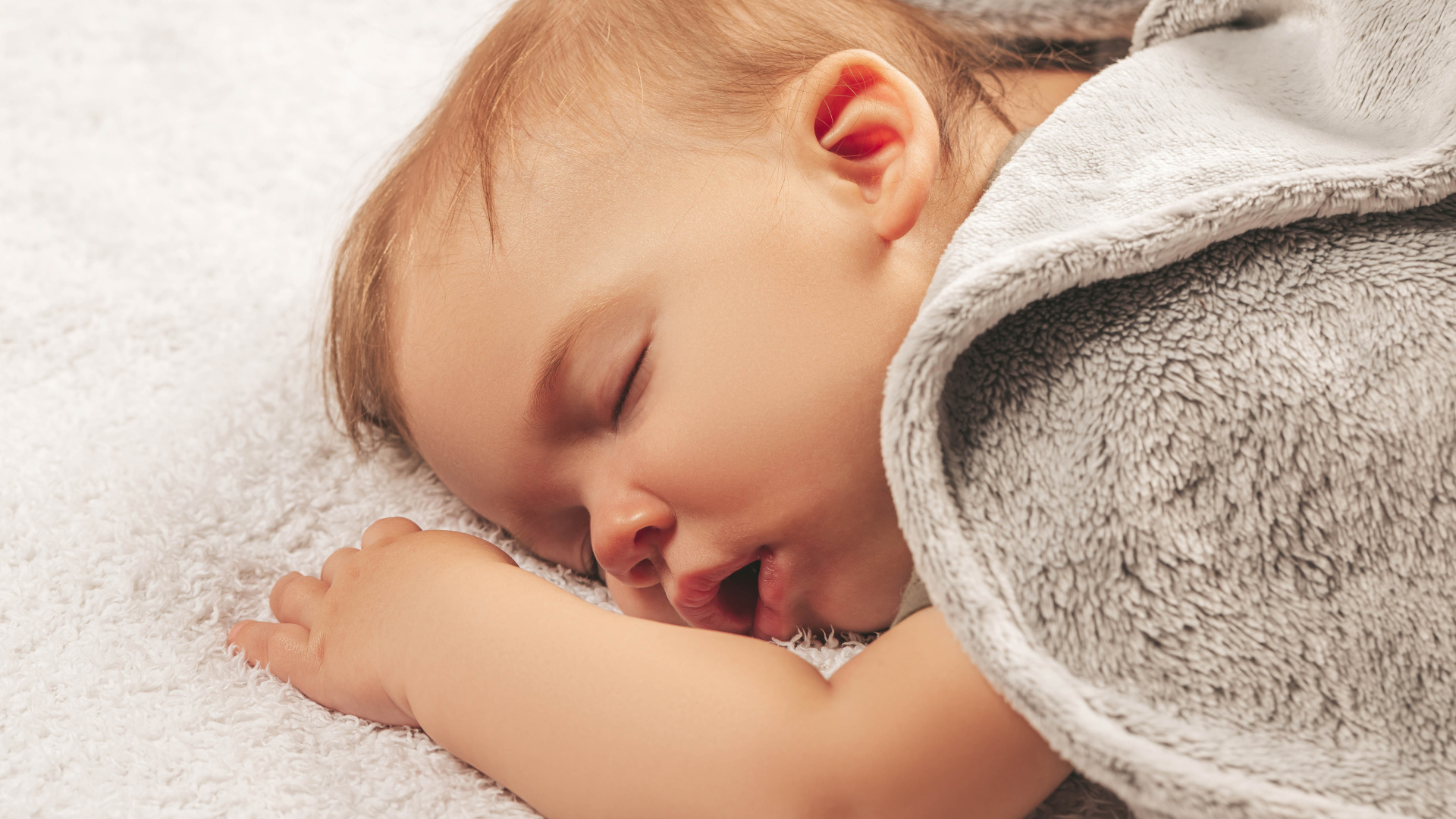 Маленький спящий ребенок под серым покрывалом 