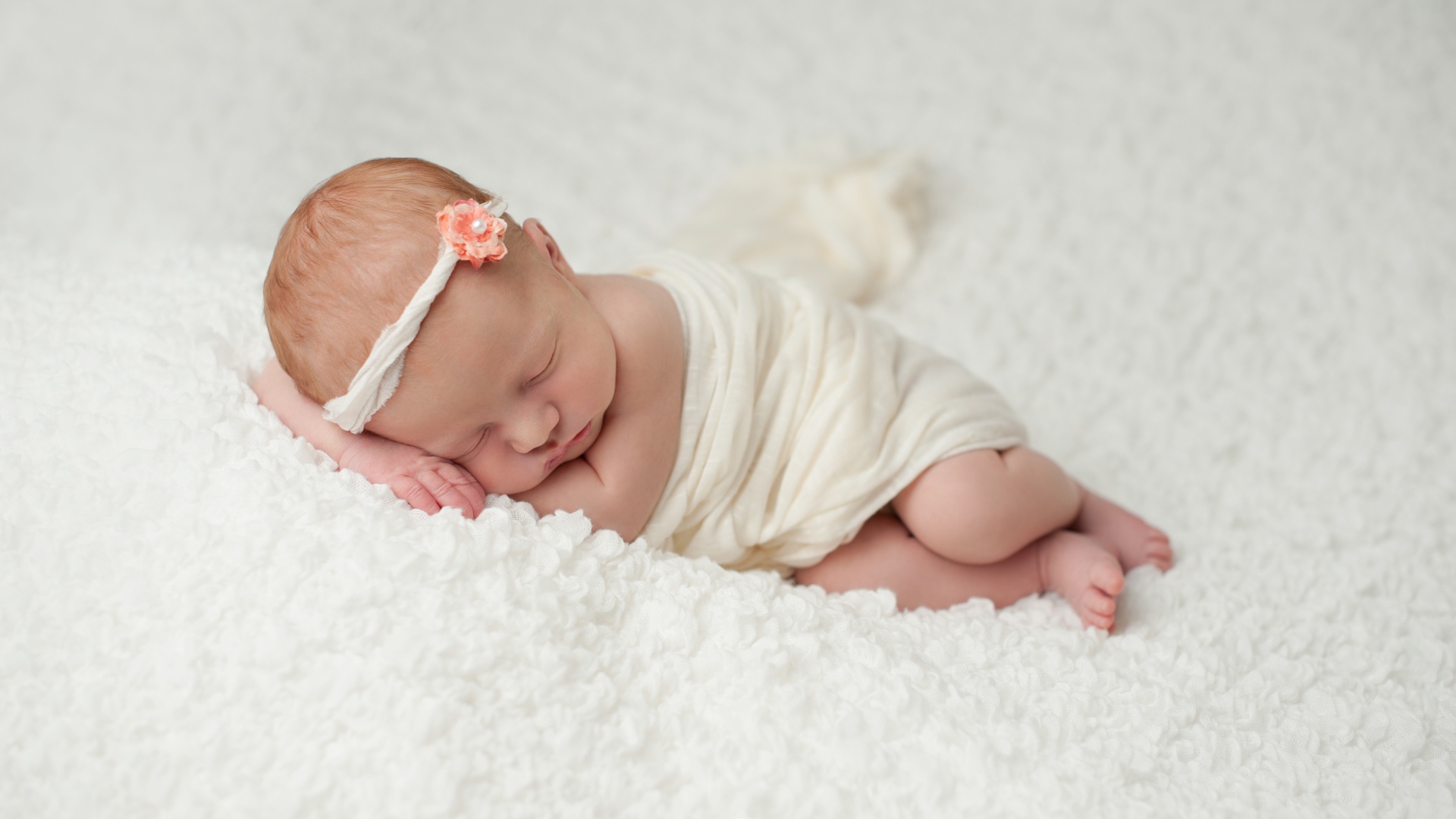 Маленький грудной ребенок спит на белом покрывале 