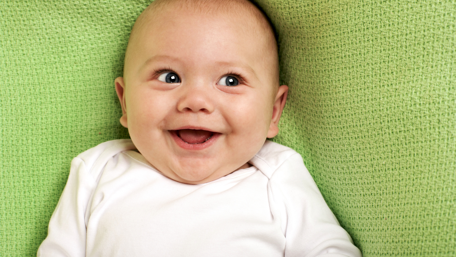 Улыбающийся маленький ребенок на зеленом покрывале 
