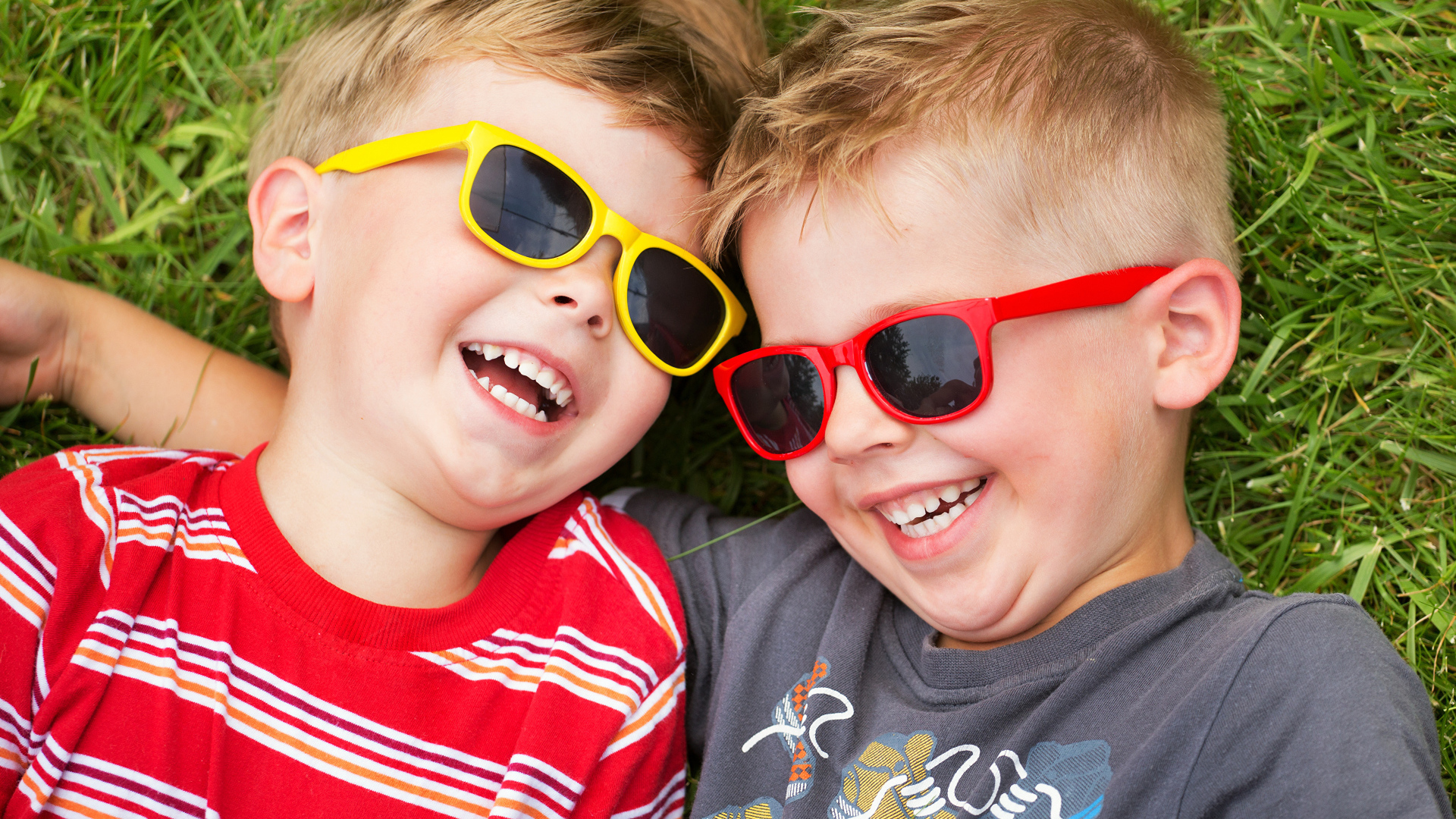 Два улыбающихся мальчика в очках на зеленой траве 