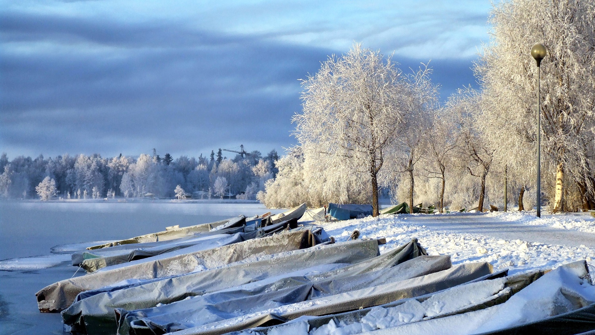 Накрытые лодки на берегу озера зимой