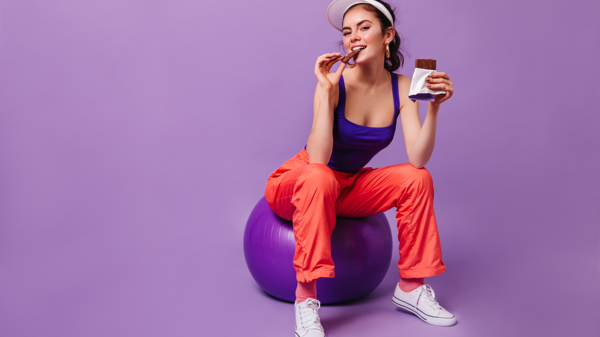 Девушка с шоколадкой сидит на фитболе