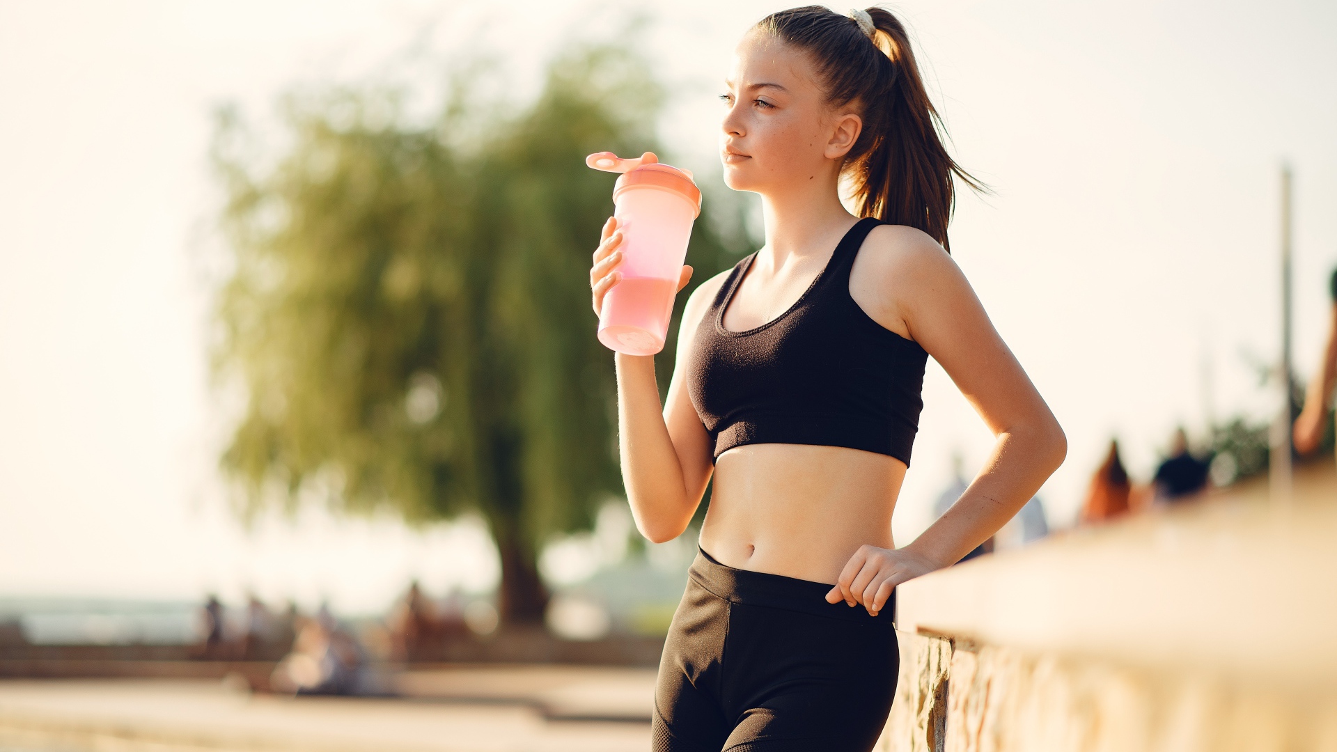 Спортивная девушка в черном пьет воду