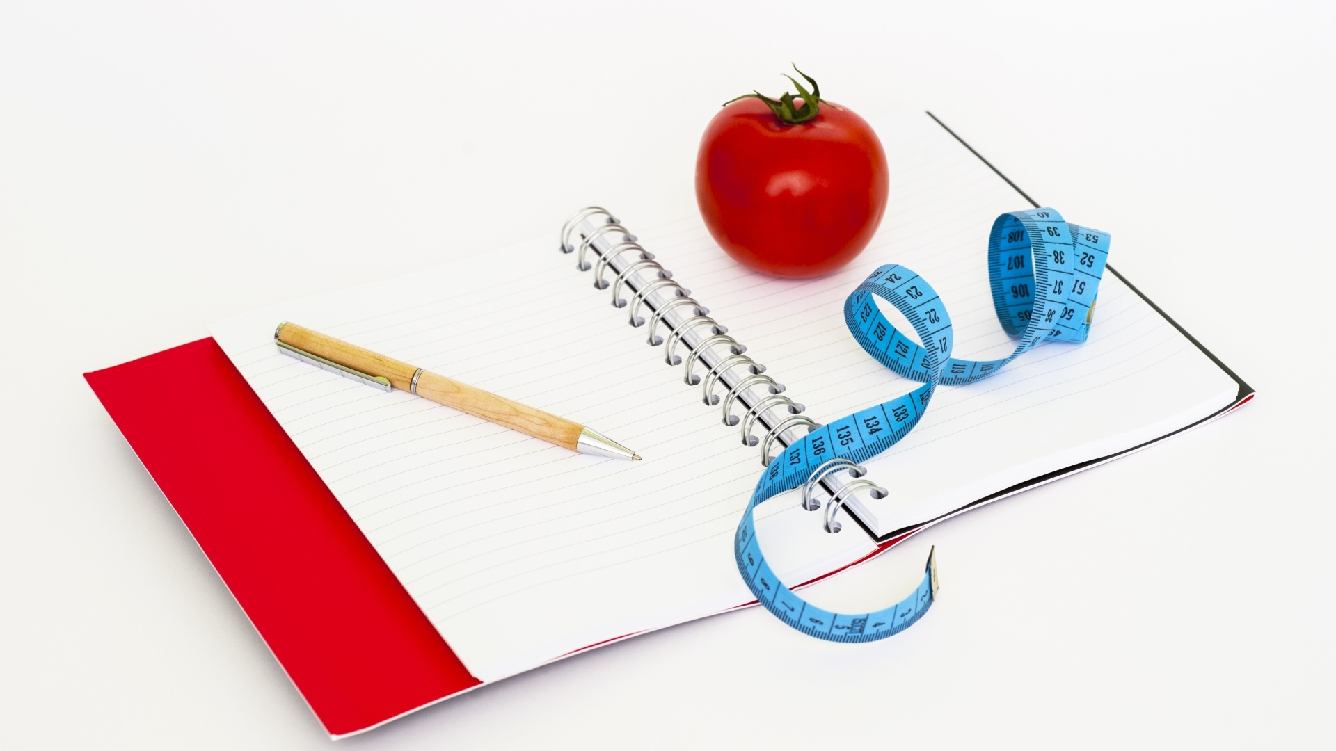 Блокнот с ручкой на столе с сантиметром и помидором