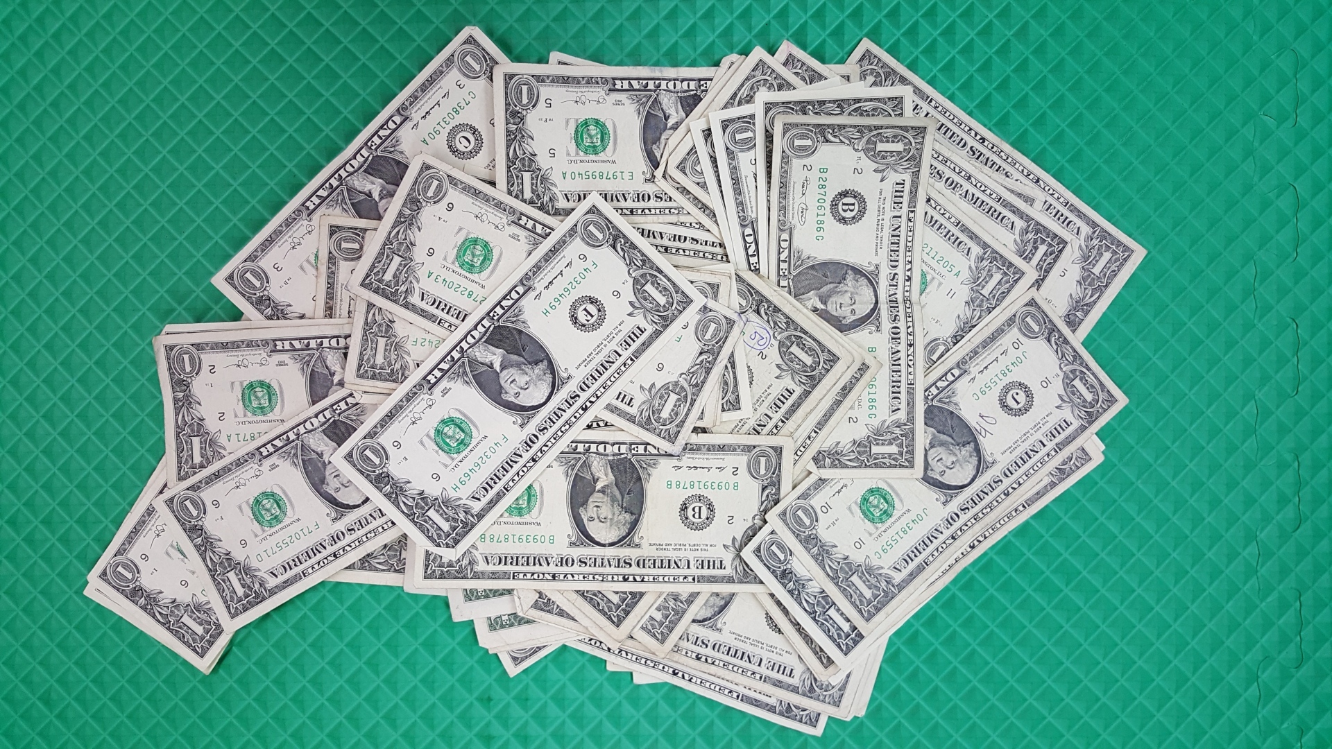 Много купюр в один доллар на зеленой поверхности