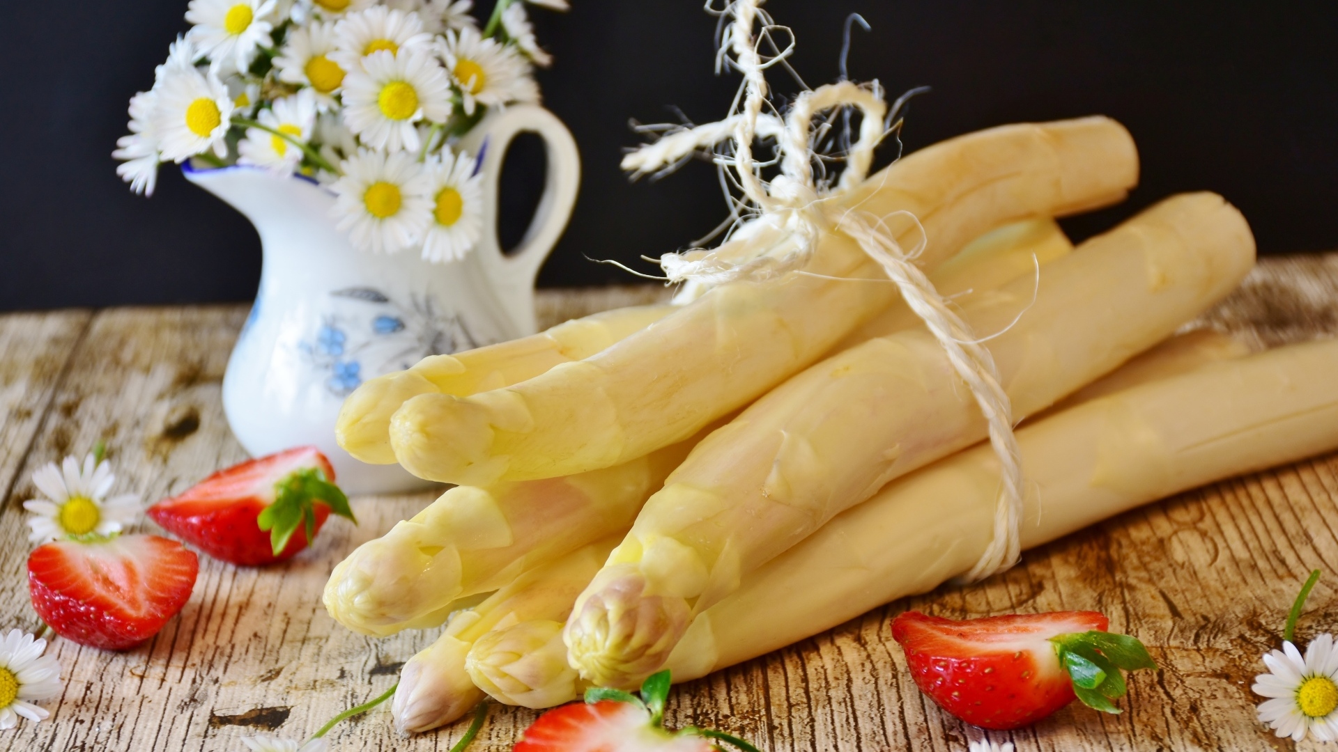 Спаржа на столе с ромашками и ягодами клубники