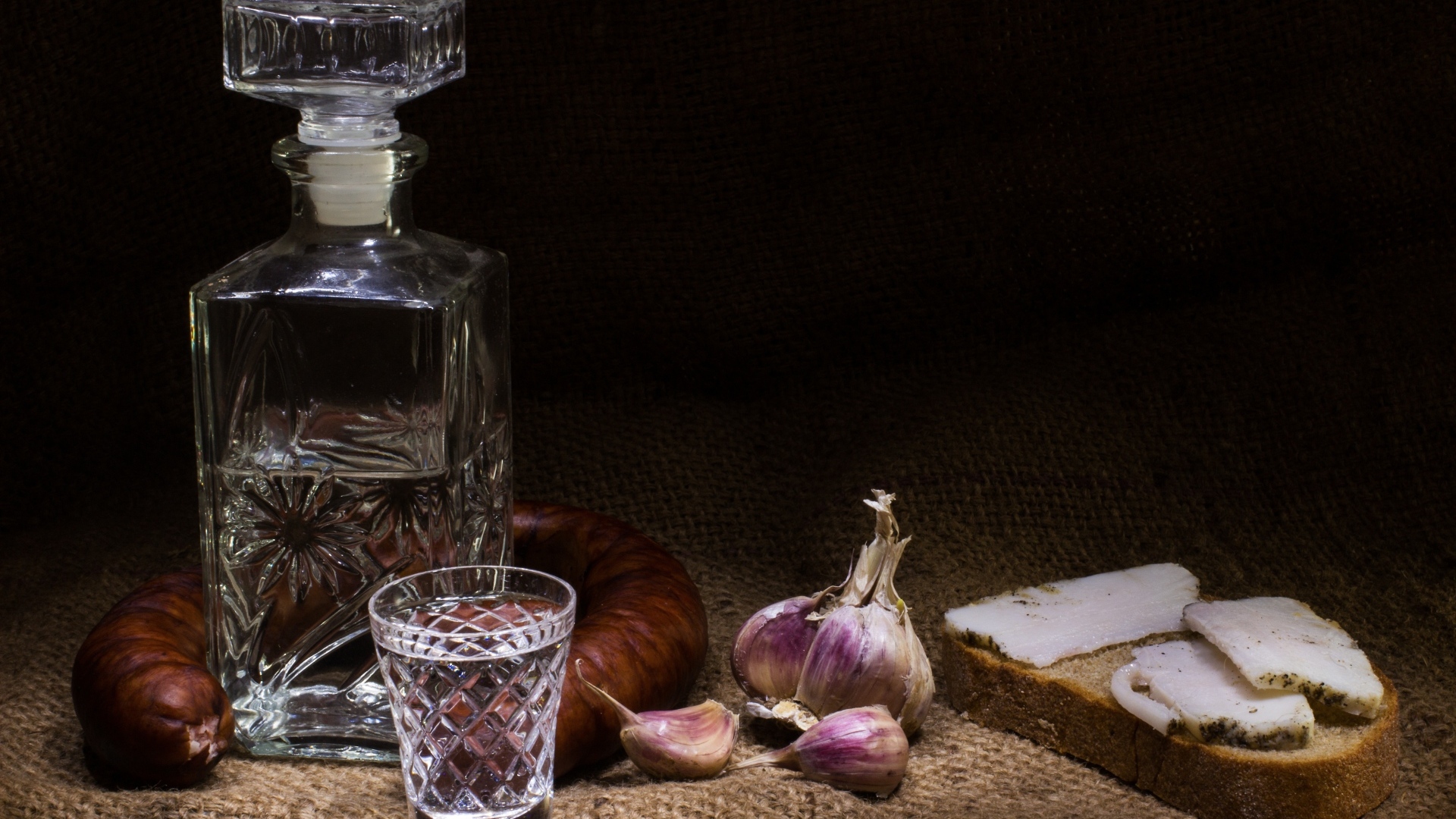 Бутылка водки на столе с салом, колбасой и чесноком