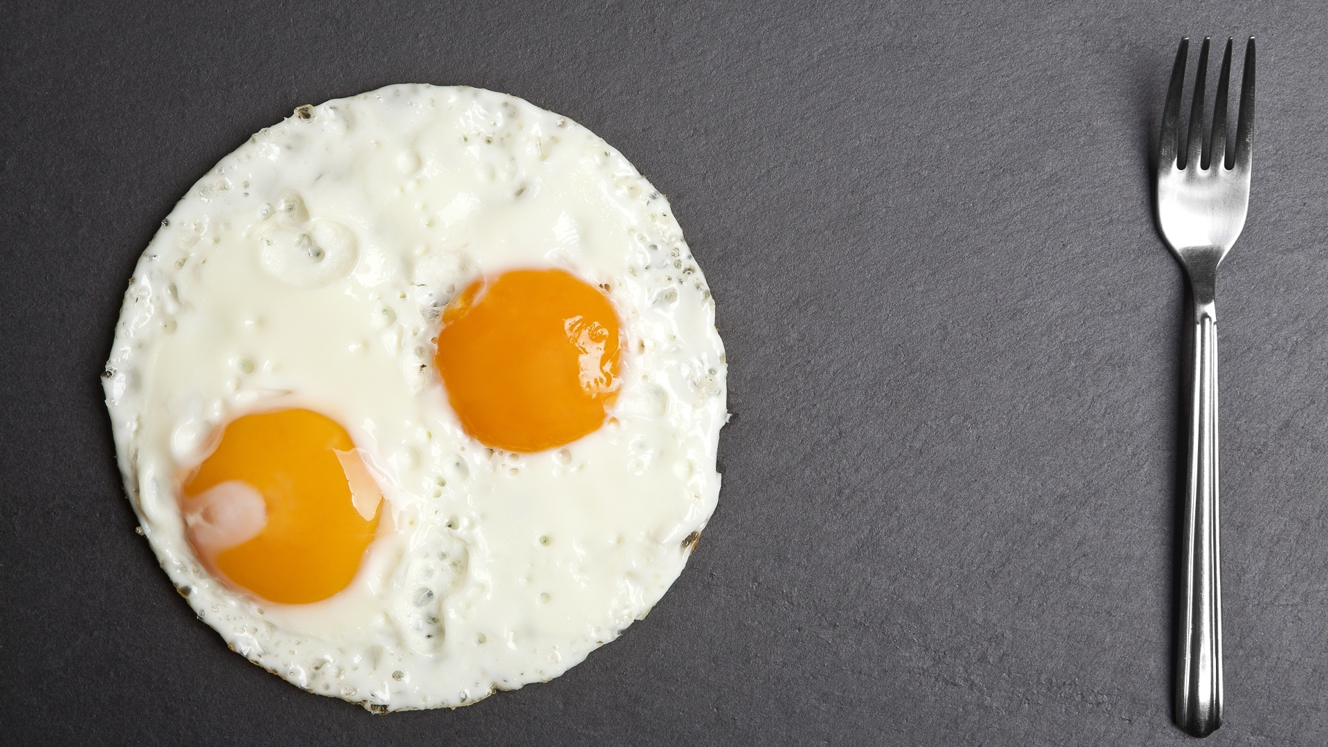 Яичница глазунья с вилкой на сером столе
