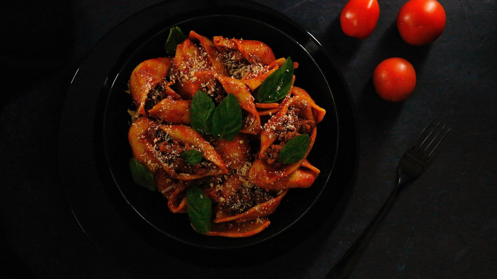 Большие макароны с фаршем в черной тарелке