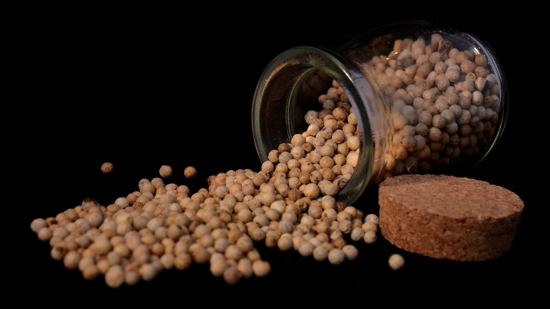 Перец горошком в банке на черном фоне