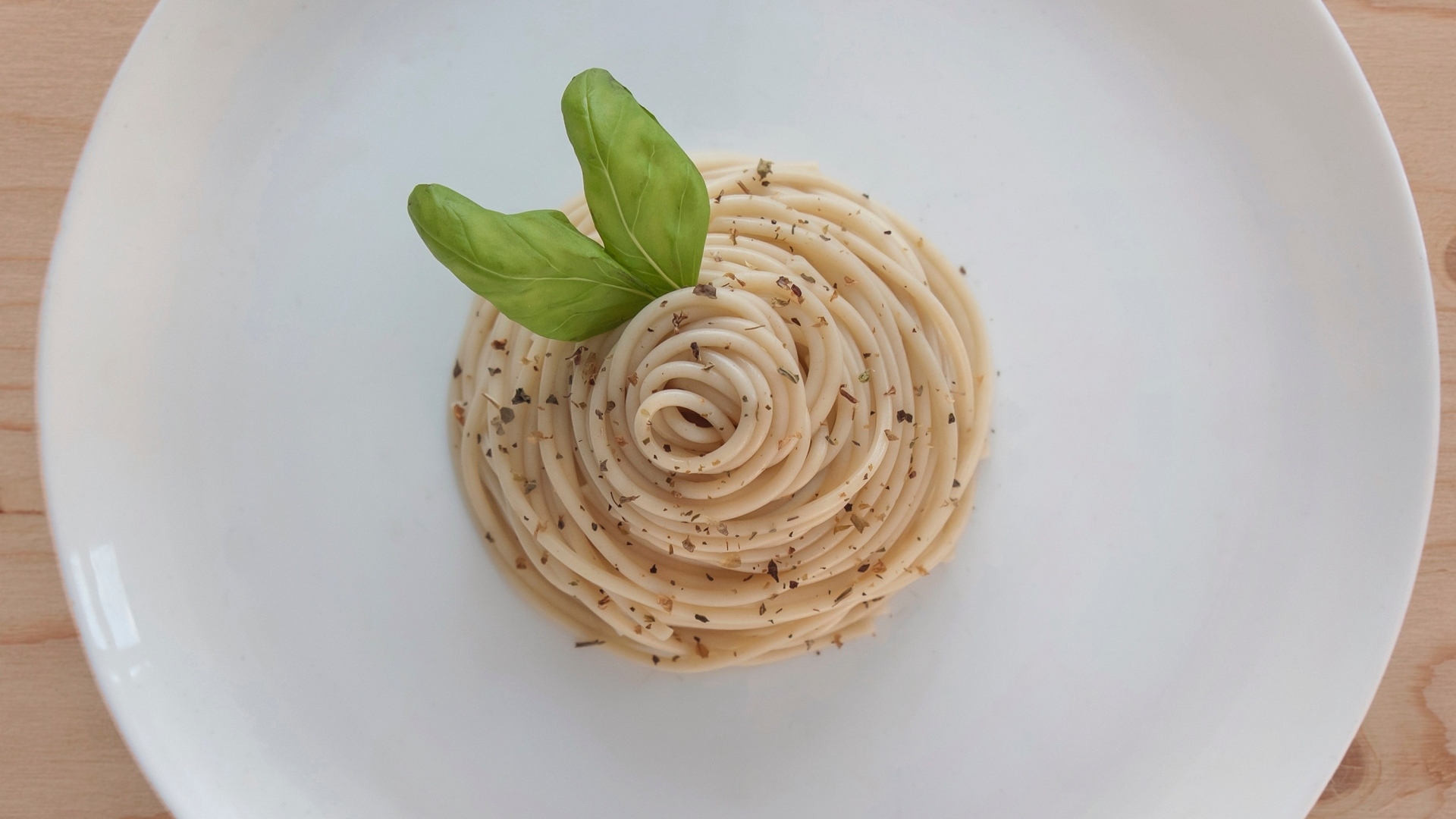 Спагетти с листьями базилика на белой тарелке