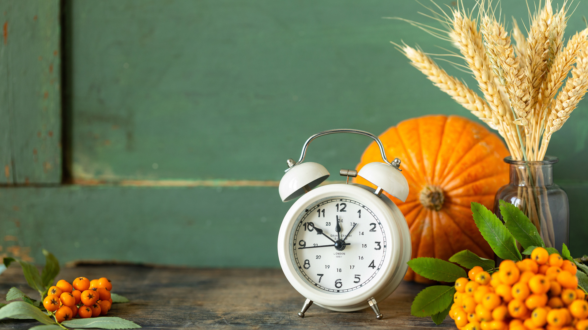 Будильник на столе с тыквой и ягодами рябины